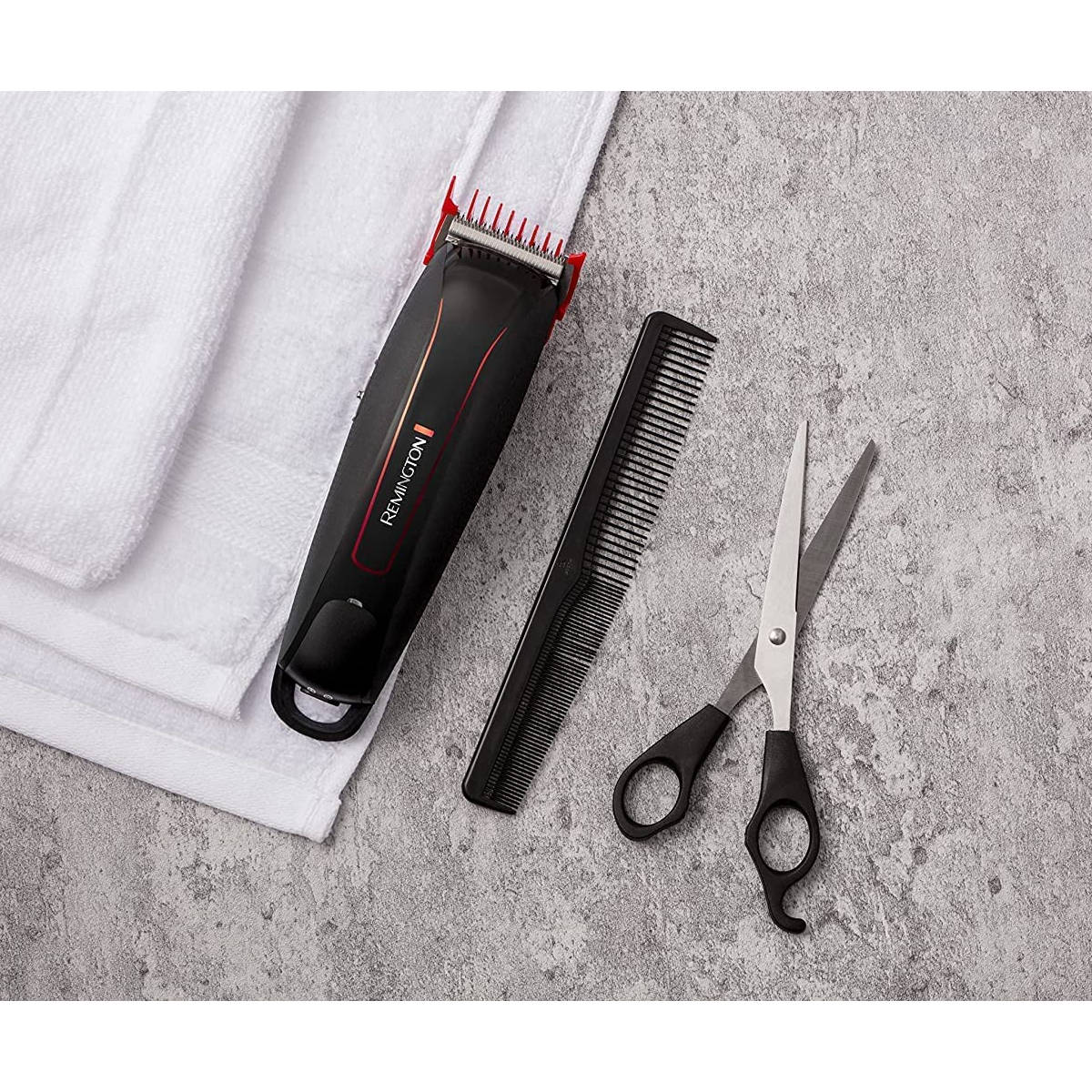 Un set per la cura del corpo con trimmer nero, pettine e forbici su una superficie strutturata, vicino ad asciugamani bianchi.