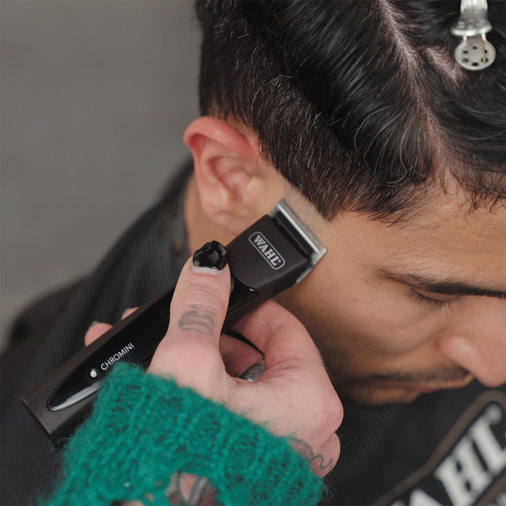 I capelli di una persona vengono tagliati con un tagliacapelli Wahl Chromini. Il tagliacapelli è nero, i capelli sono scuri.