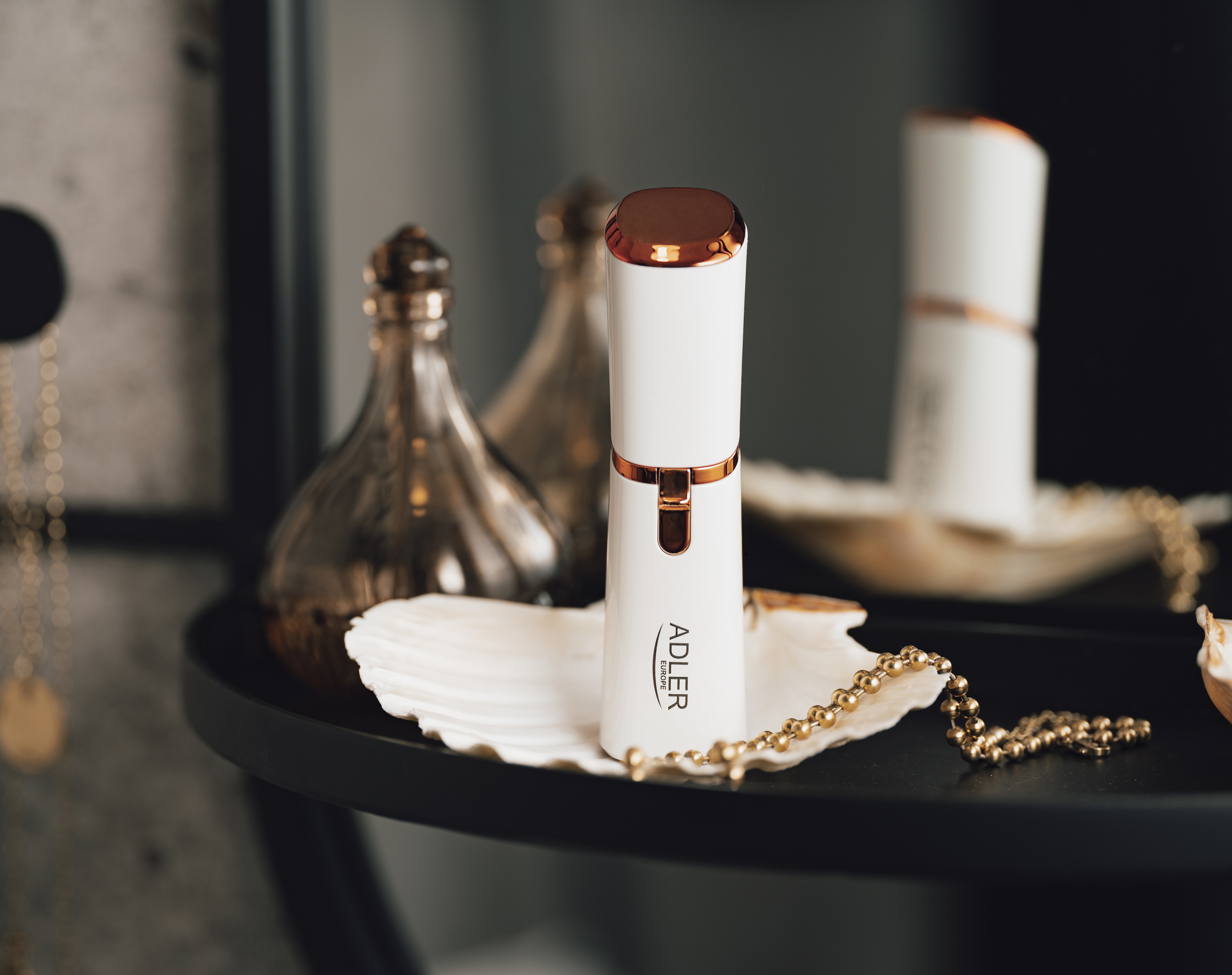 Prodotto di bellezza bianco e rame. Posizionato in una conchiglia su una superficie scura. Catena d'oro e bottiglie decorative vicine.