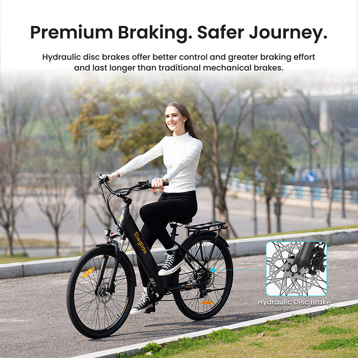 Kobieta jedzie rowerem elektrycznym po utwardzonej drodze. Rower ma hydrauliczne hamulce tarczowe. Tło przedstawia drzewa i zachmurzone niebo.