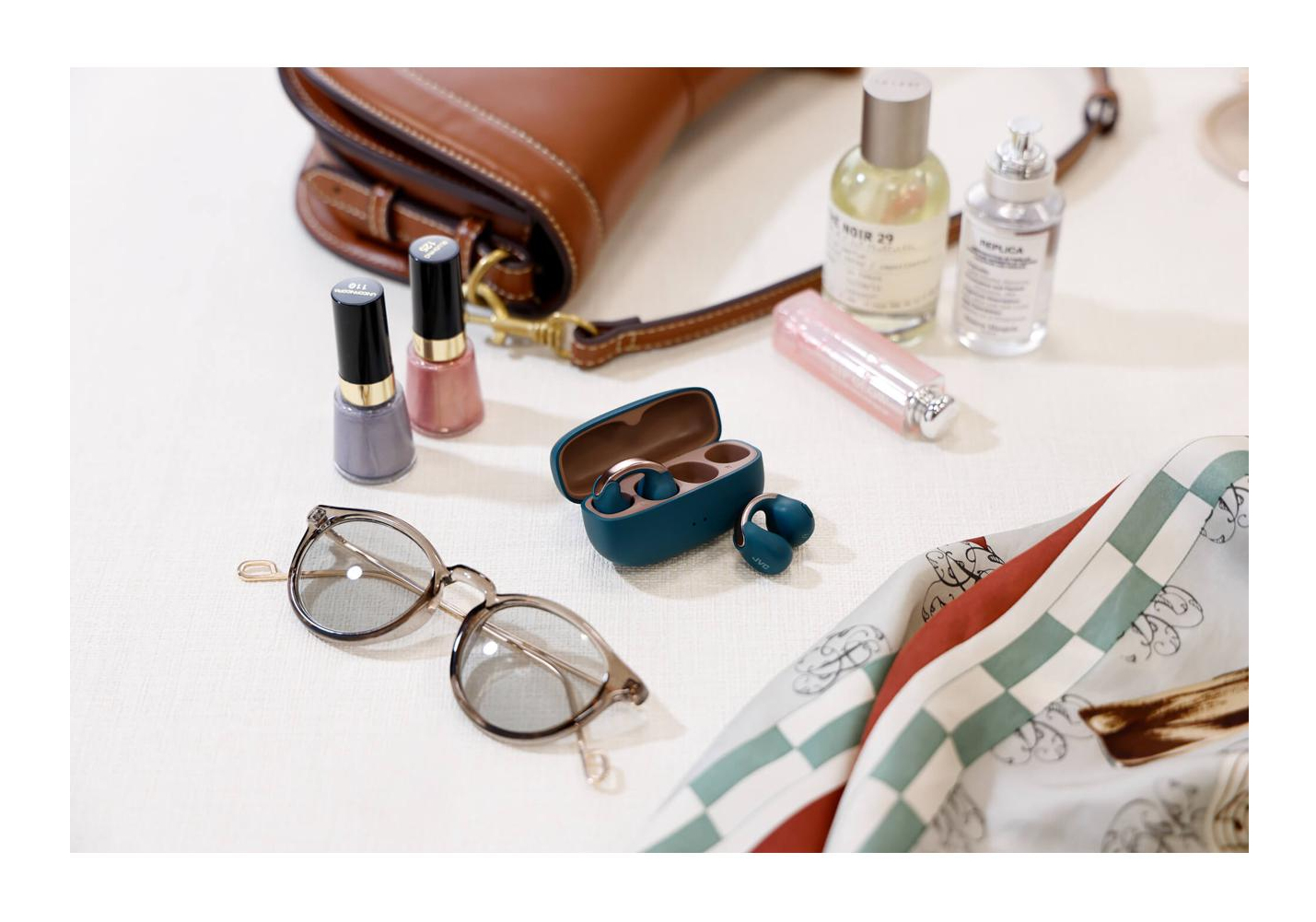 Okulary przeciwsłoneczne, lakier do paznokci, perfumy, słuchawki, szminka, torebka i szalik na białej powierzchni.