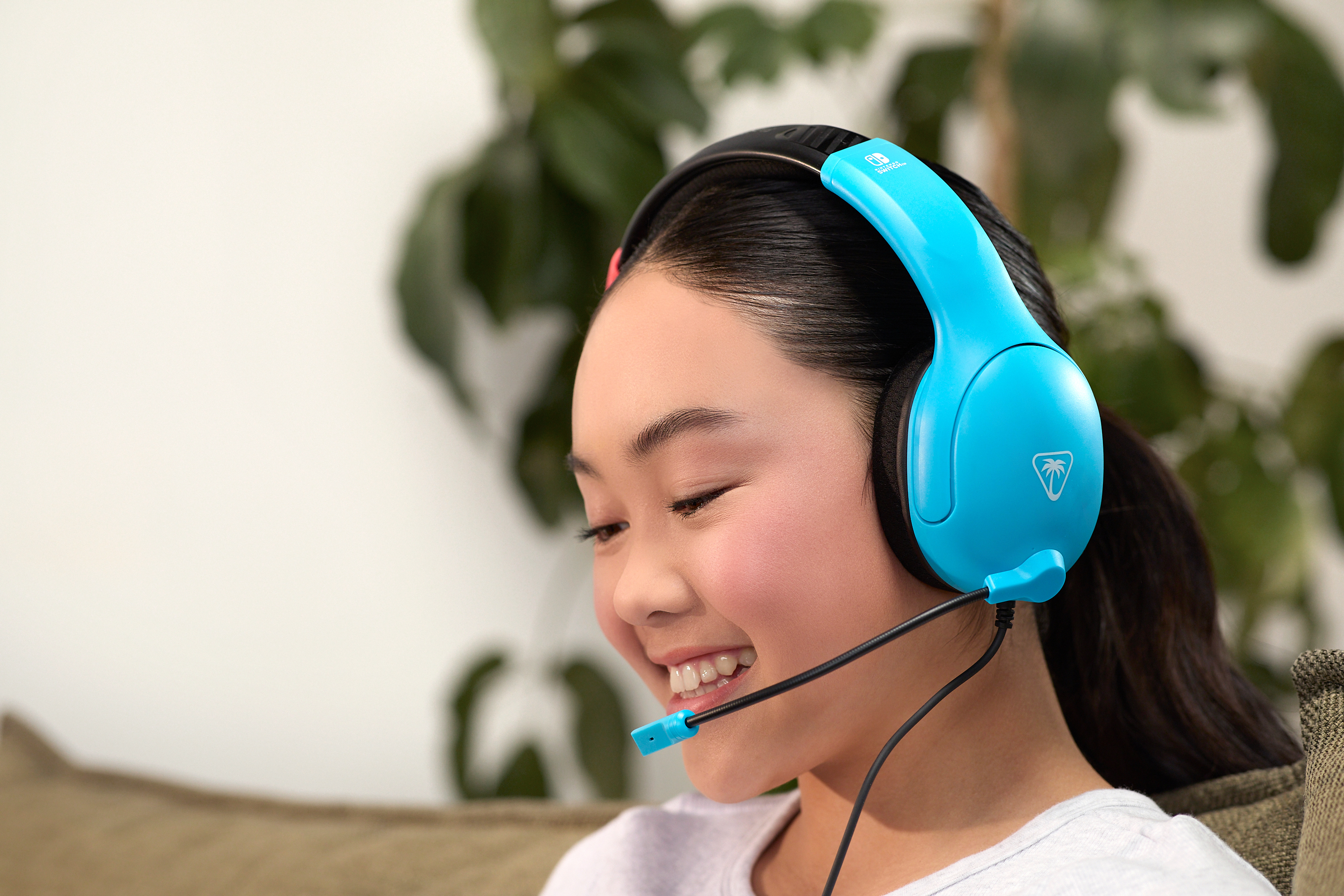 Een jonge vrouw glimlacht met een blauwe headset met microfoon. Groene planten op de achtergrond.