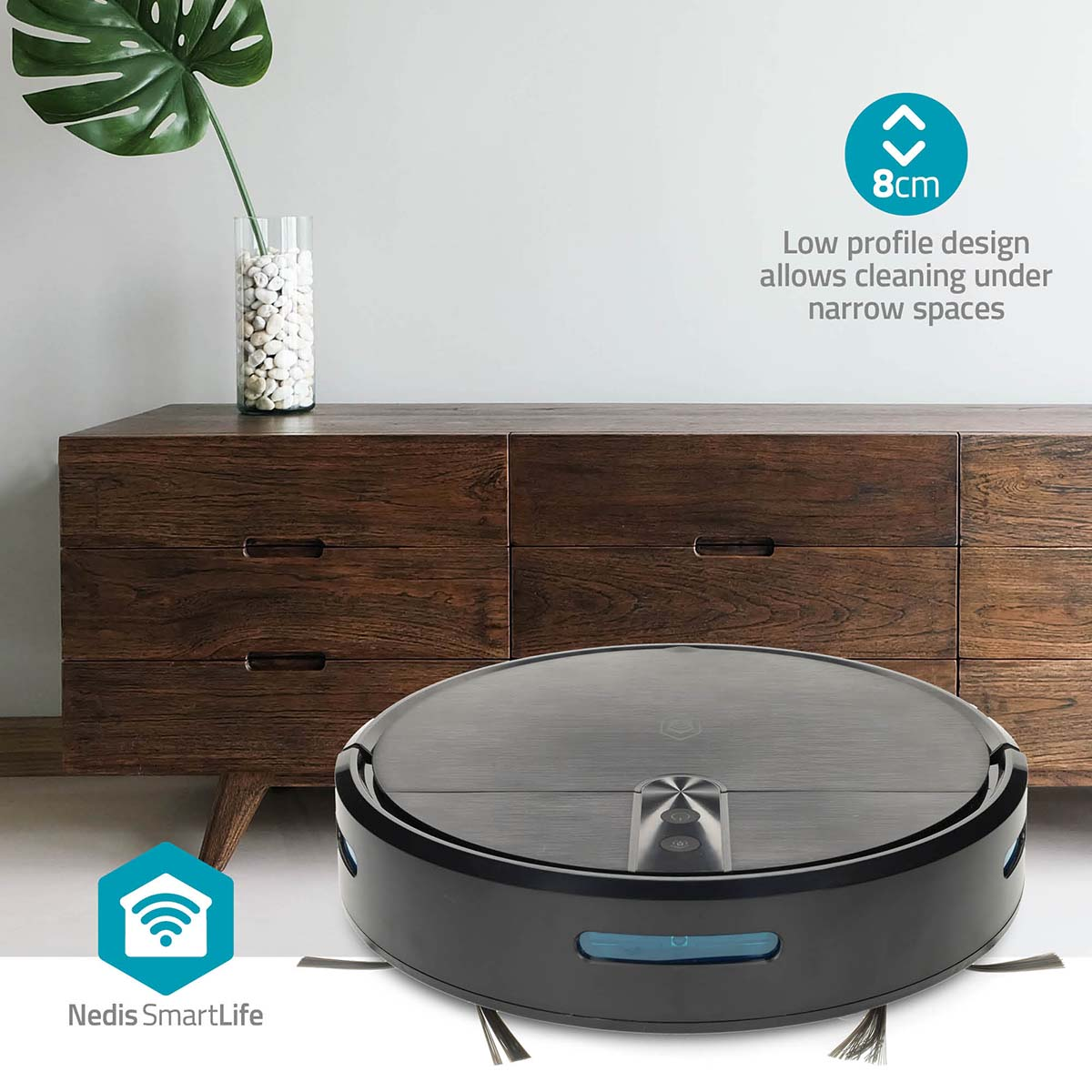 Un aspirapolvere robot nero su un pavimento bianco. Sullo sfondo, un mobile in legno con una pianta.