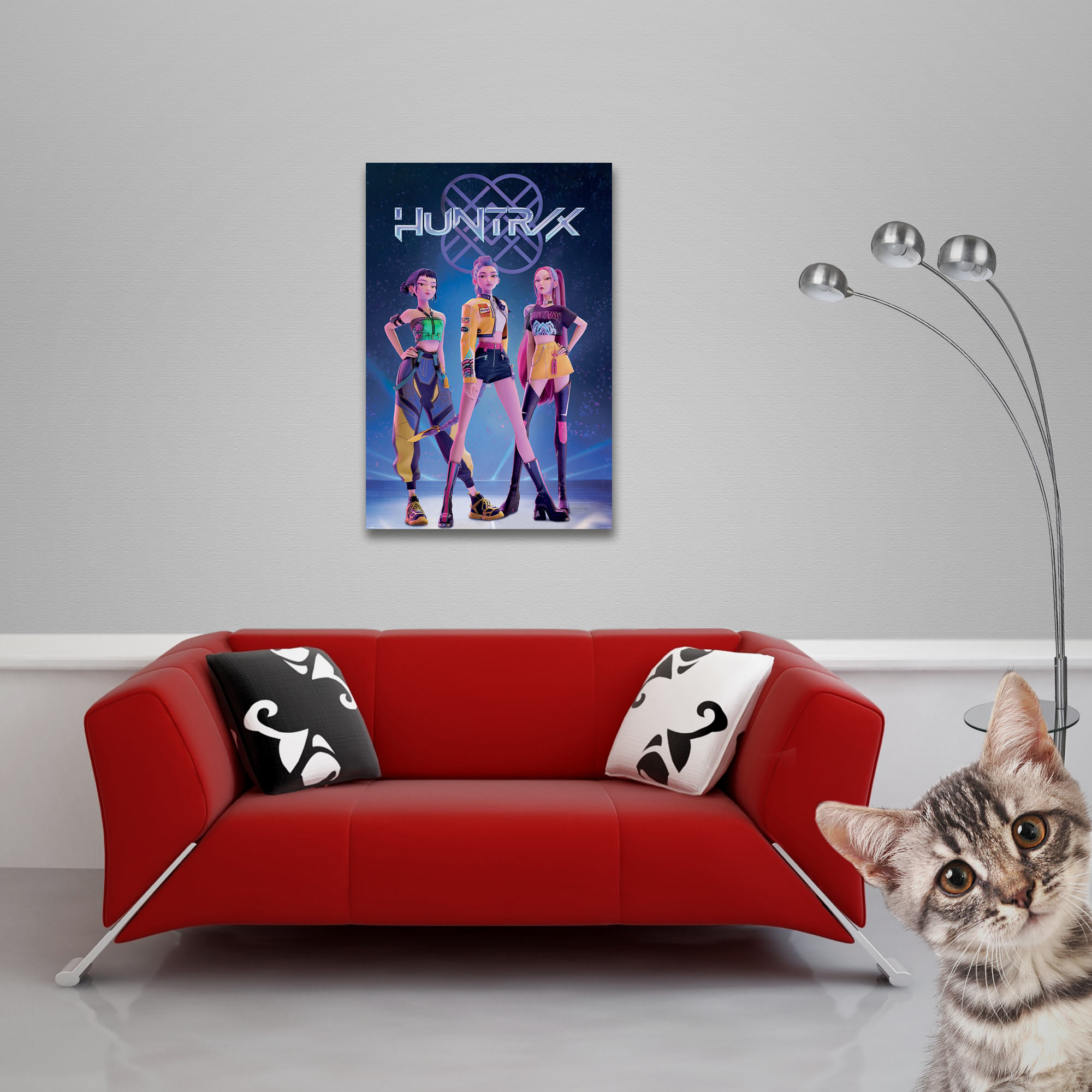 Ein rotes Sofa mit Zierkissen und ein Poster mit Frauen. Eine Katze schaut aus der Ecke.