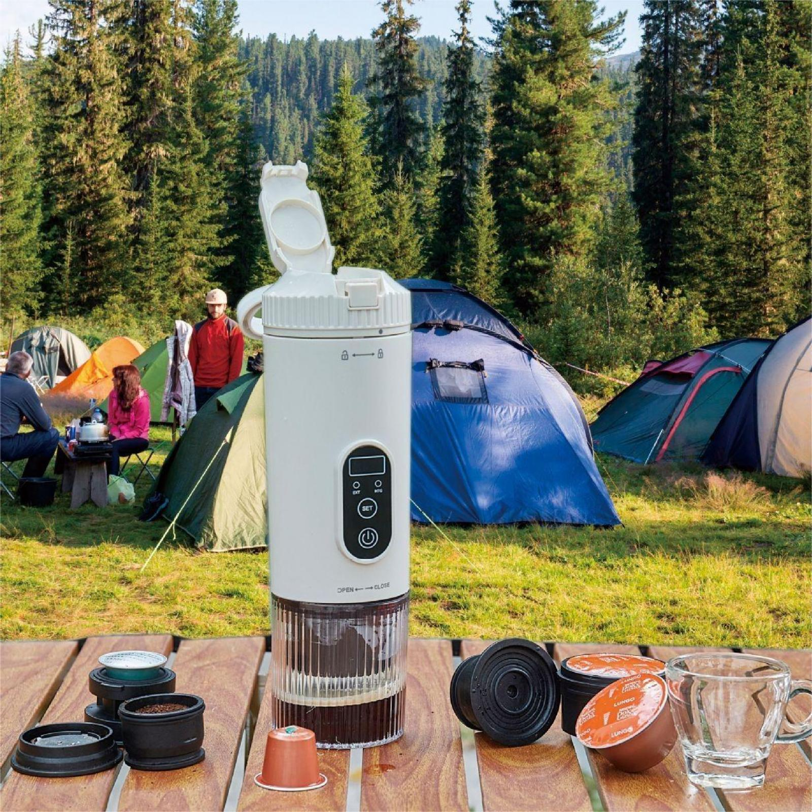 Kaffeemaschine in einer Campingszene. Zelte und Menschen sind im Hintergrund. Kaffeepads und eine Tasse stehen auf einem Holztisch.