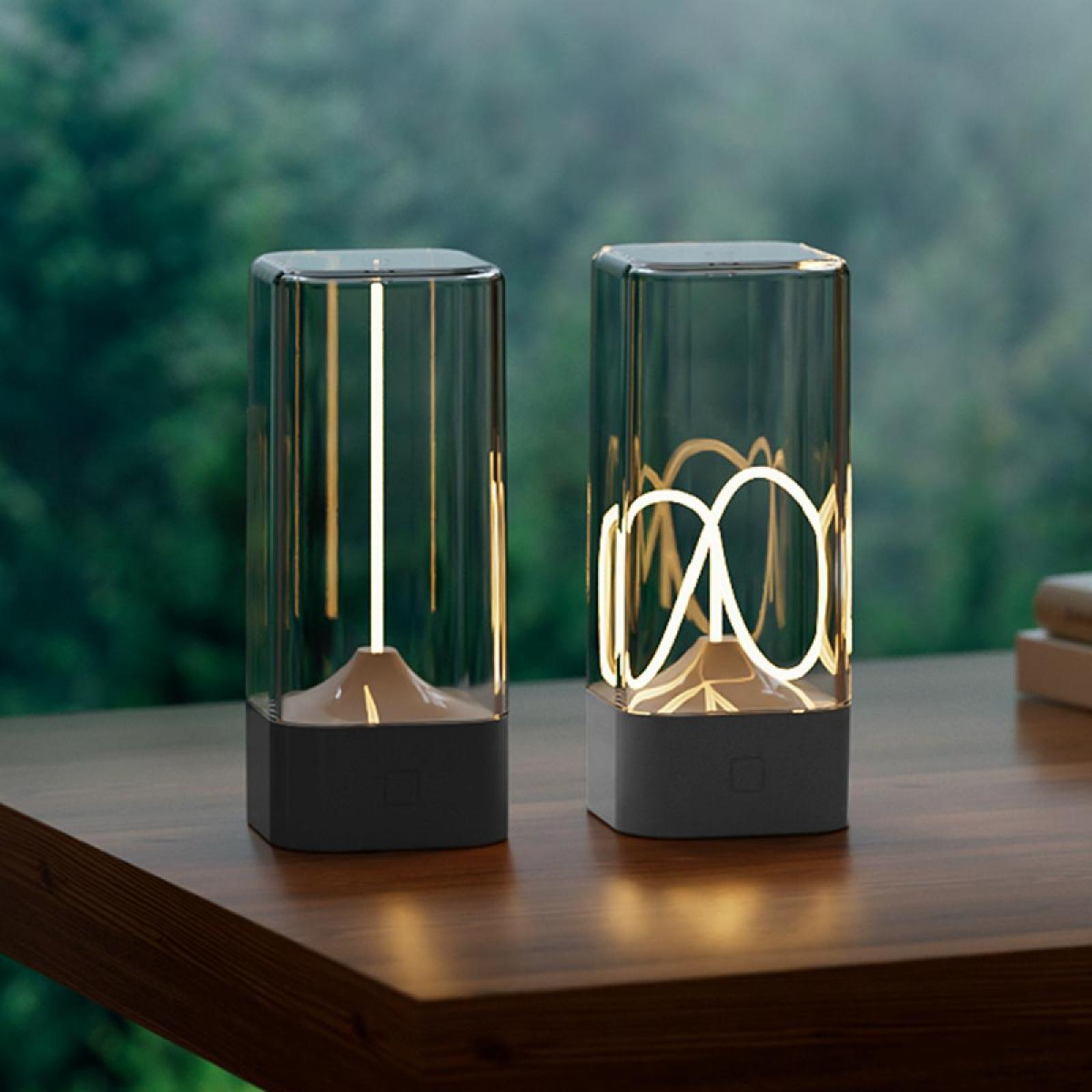 Zwei moderne Lampen mit beleuchteten Designs stehen auf einem Holztisch. Hintergrund sind verschwommene grüne Bäume.