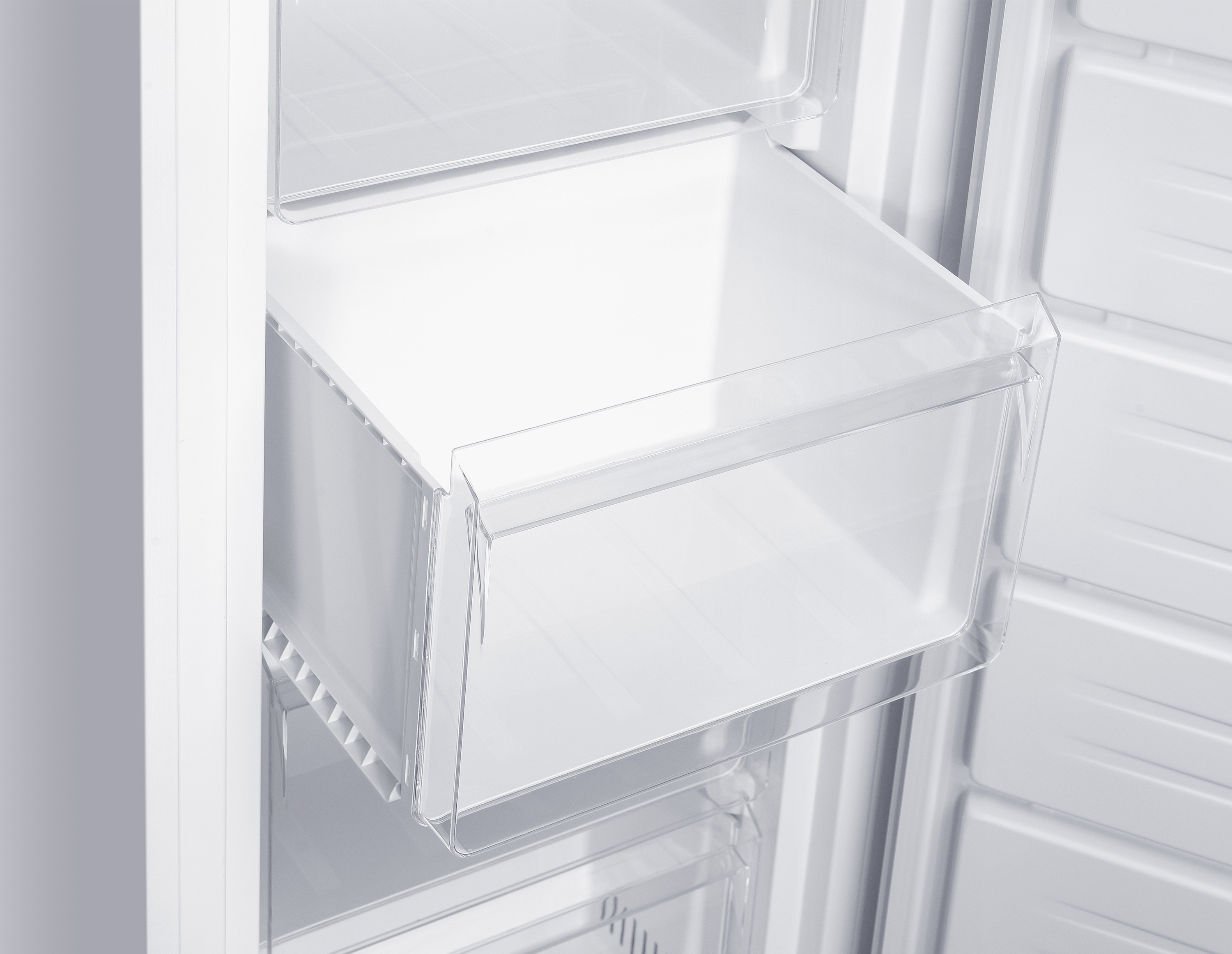 In einem weißen Kühlschrank ist eine transparente Schublade herausgezogen. Die Schublade ist leer. Der Hintergrund ist weiß.