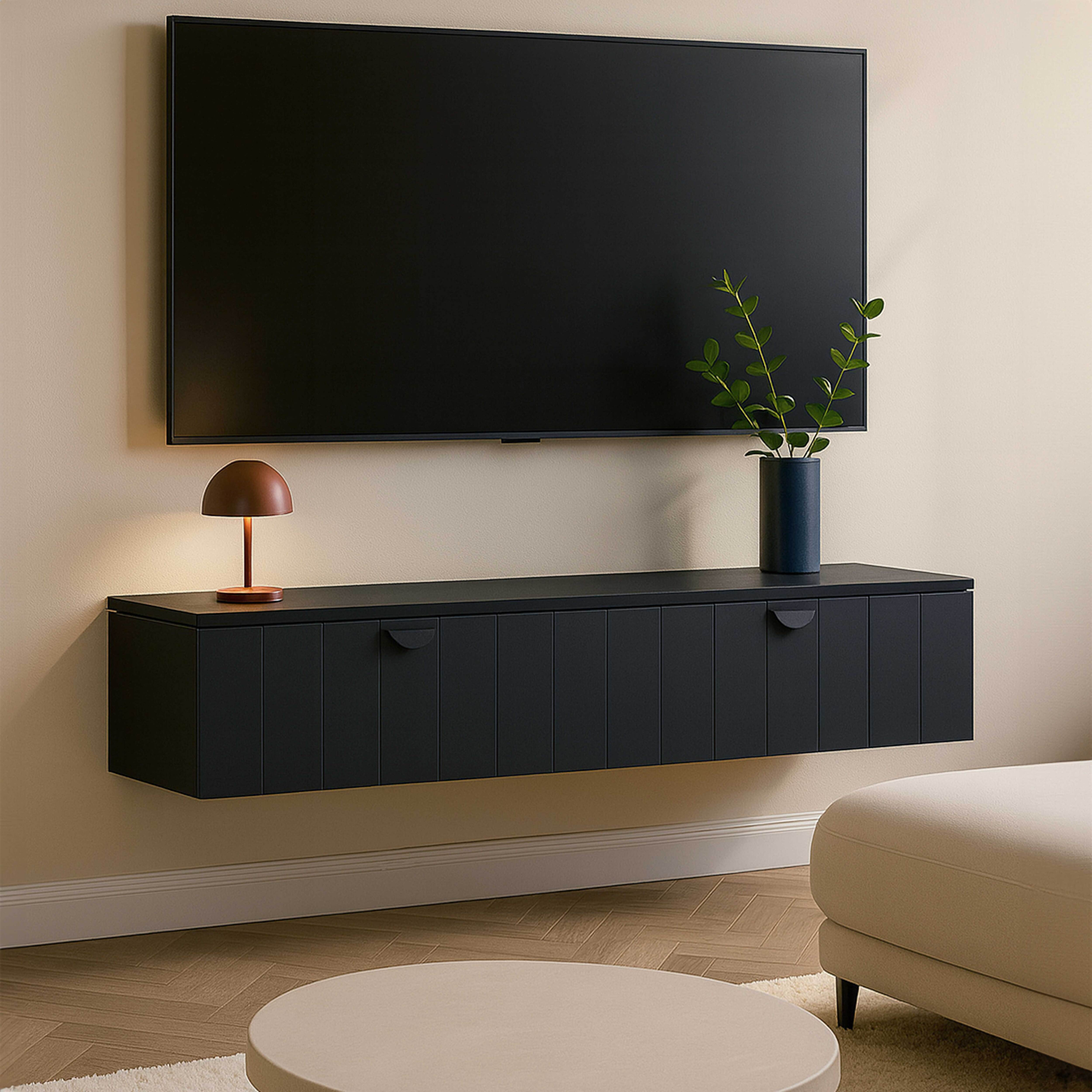 Ein schwarzer Fernseher über einem schwarzen Schrank mit Lampe, Vase mit Blättern, rundem Tisch und Sofa.