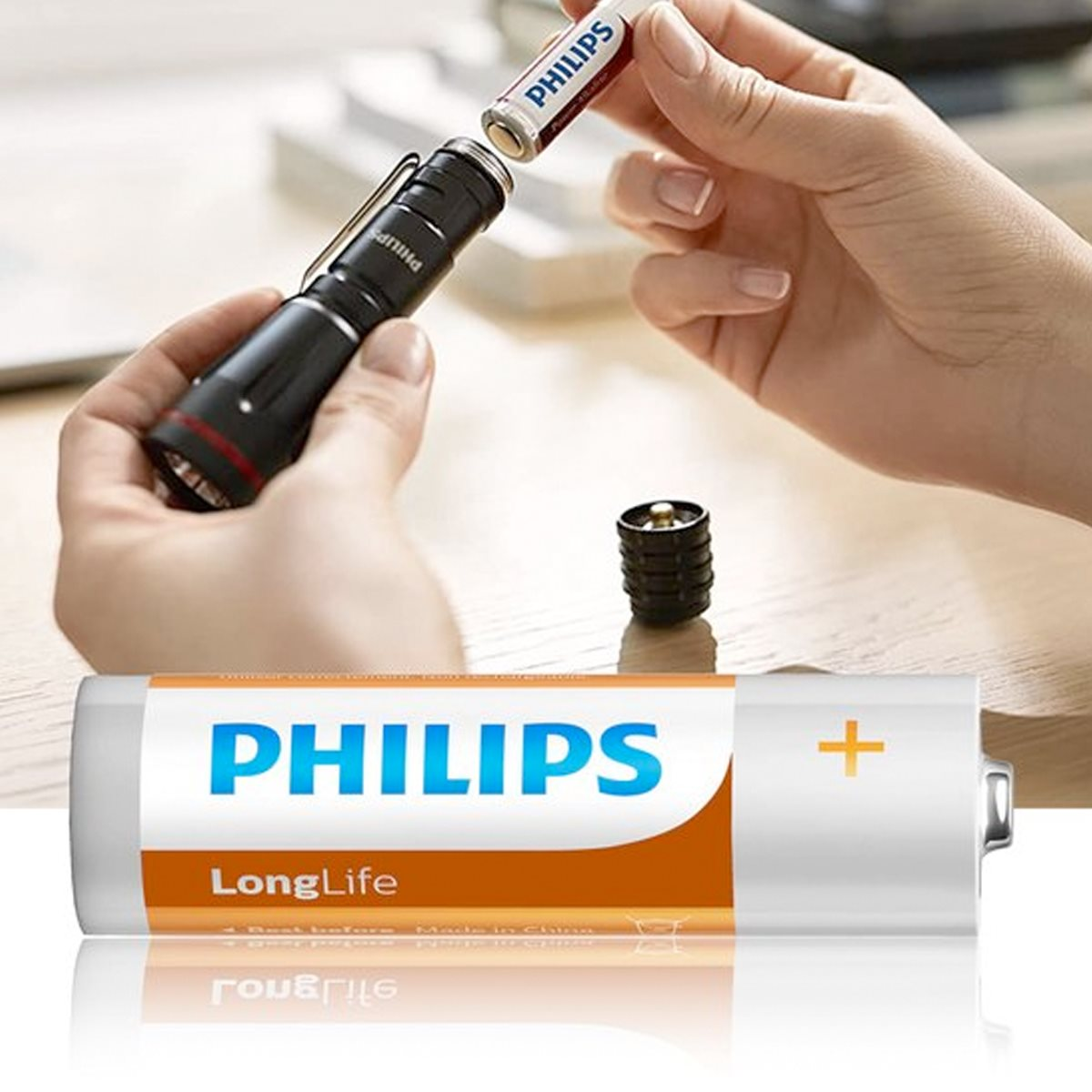 Hände legen eine Philips-Batterie in eine schwarze Taschenlampe ein. Eine große Philips-Batterie und eine zusätzliche Batterie sind ebenfalls sichtbar.