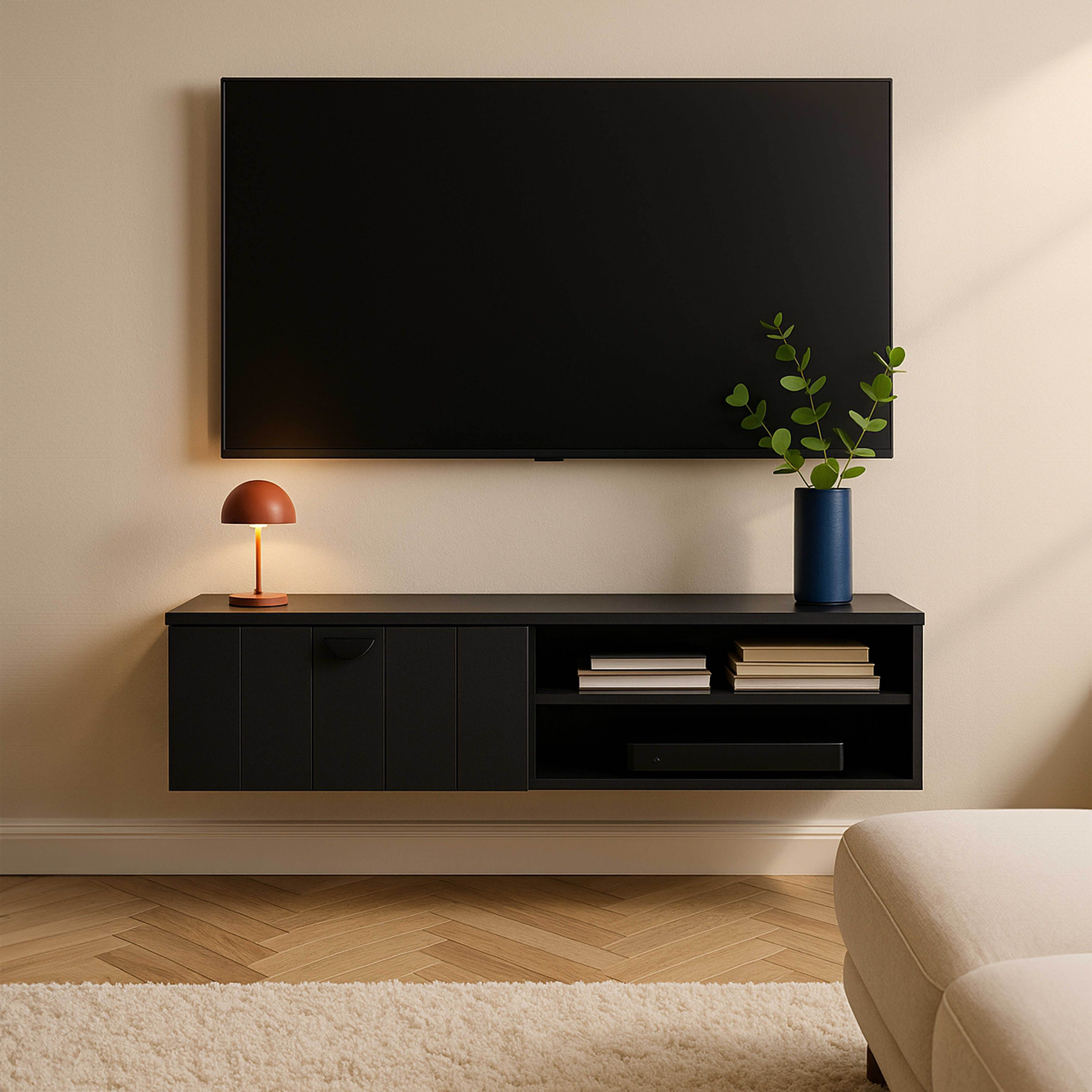 Ein schwarzer Fernseher über einem schwarzen Schrank mit Lampe, blauer Vase und Büchern. Teppich und Sofa sind zu sehen.