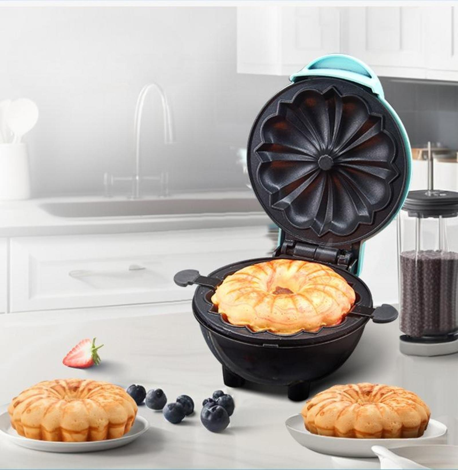 Ein Donut-Maker mit einem gekochten Donut, zwei Donuts auf Tellern, Blaubeeren und eine Erdbeere auf der Theke.