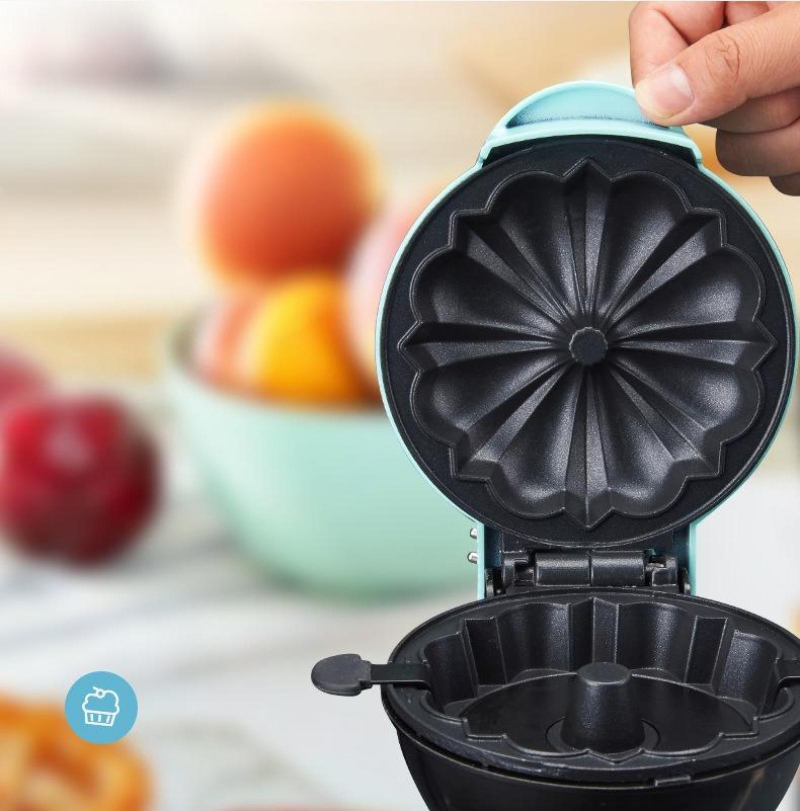 Ein Mini-Gugelhupf-Maker ist geöffnet und zeigt einen Antihaft-Innenraum. Obst und eine Schüssel sind im Hintergrund unscharf.