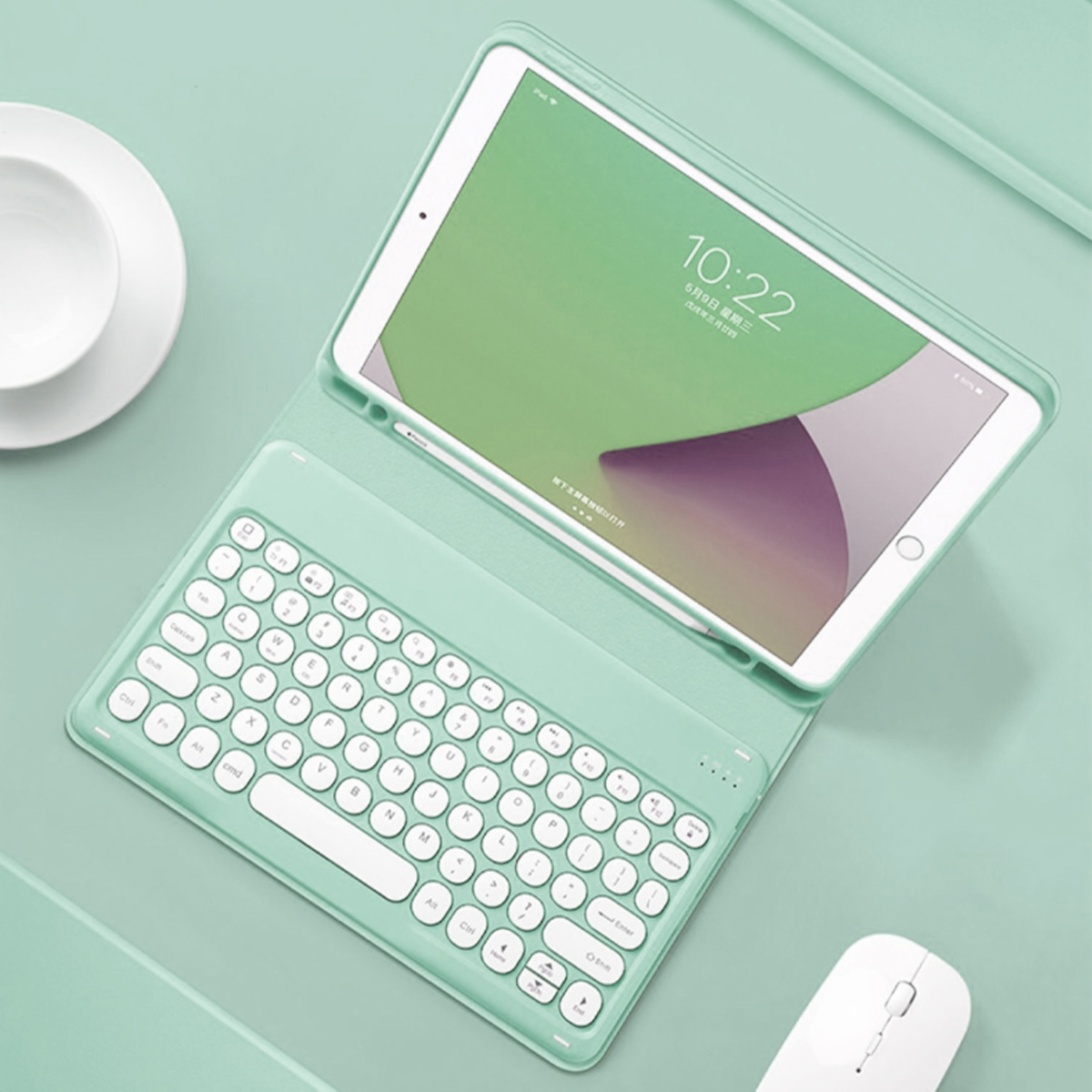 Ein Tablet mit angeschlossener Tastatur und Hülle, eine Tasse und eine weiße Maus auf einer grünen Oberfläche. Der Tablet-Bildschirm zeigt die Uhrzeit.