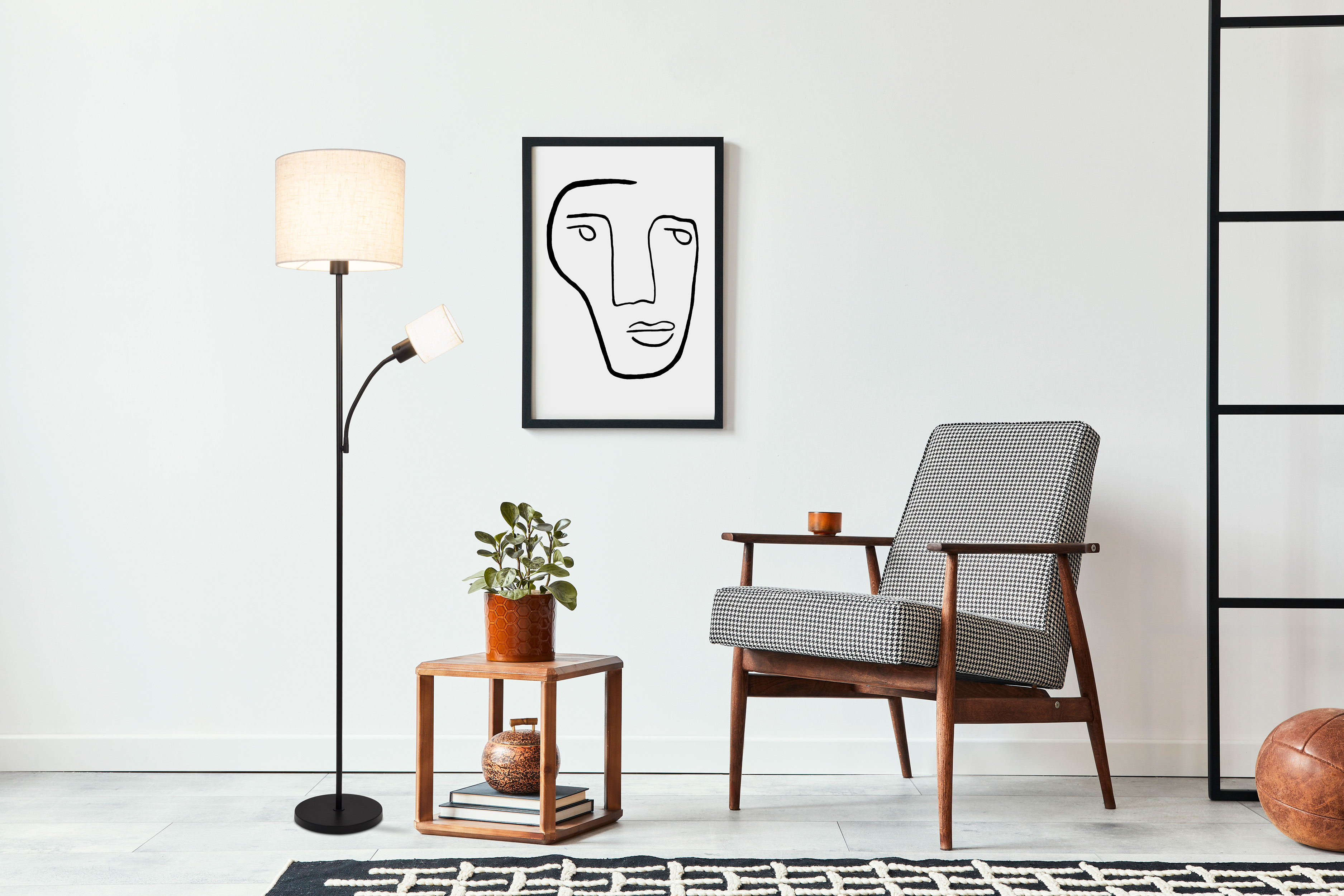Zimmer mit moderner Einrichtung: Sessel, Stehlampe, Beistelltisch mit Pflanze, Kunstwerk, Teppich und Lederball.