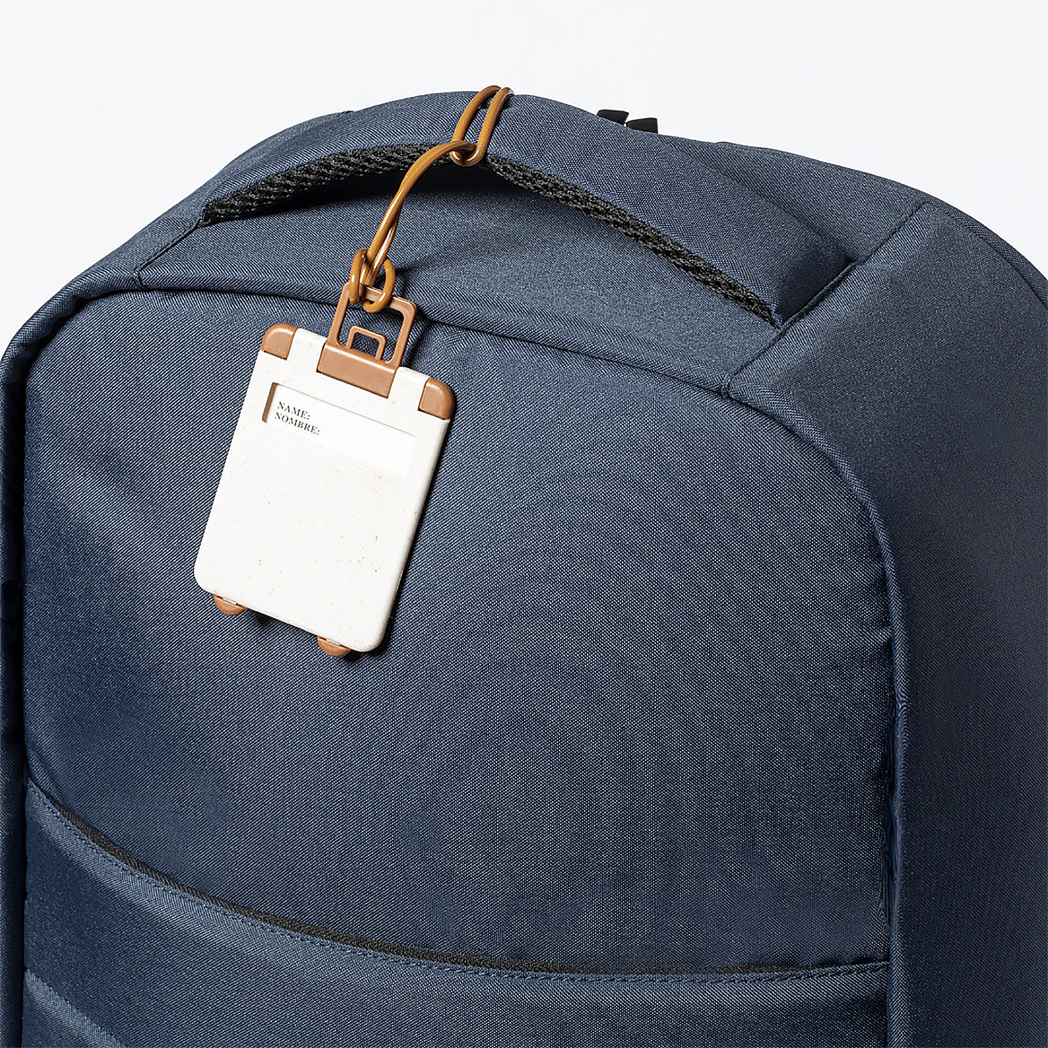 Una mochila azul oscuro con una etiqueta de equipaje adjunta. La etiqueta es blanca con marco marrón y dice 'NAME: NOMBRE:'.
