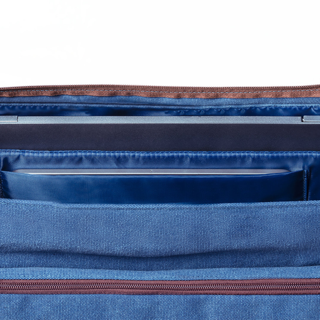 Primo piano dell'interno di una borsa blu per laptop. Gli strati visibili includono un laptop, tasche e una cerniera marrone.