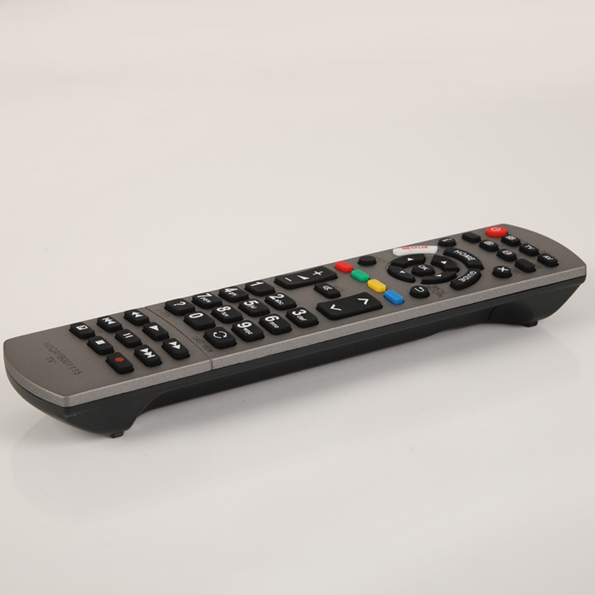 Eine graue TV-Fernbedienung mit vielen Tasten liegt auf einer weißen Oberfläche. Die Tasten haben verschiedene Farben und Beschriftungen.