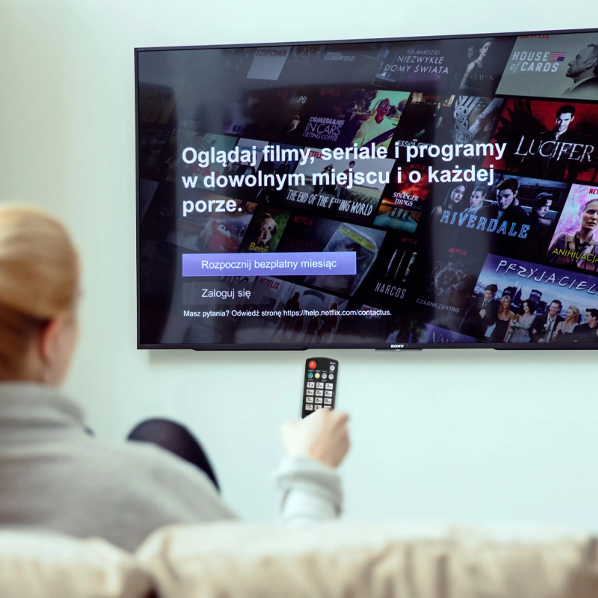 Eine Person sieht sich Netflix auf einem großen Fernseher an. Die Fernbedienung ist in der Hand. Der Bildschirm zeigt verschiedene Sendungen.