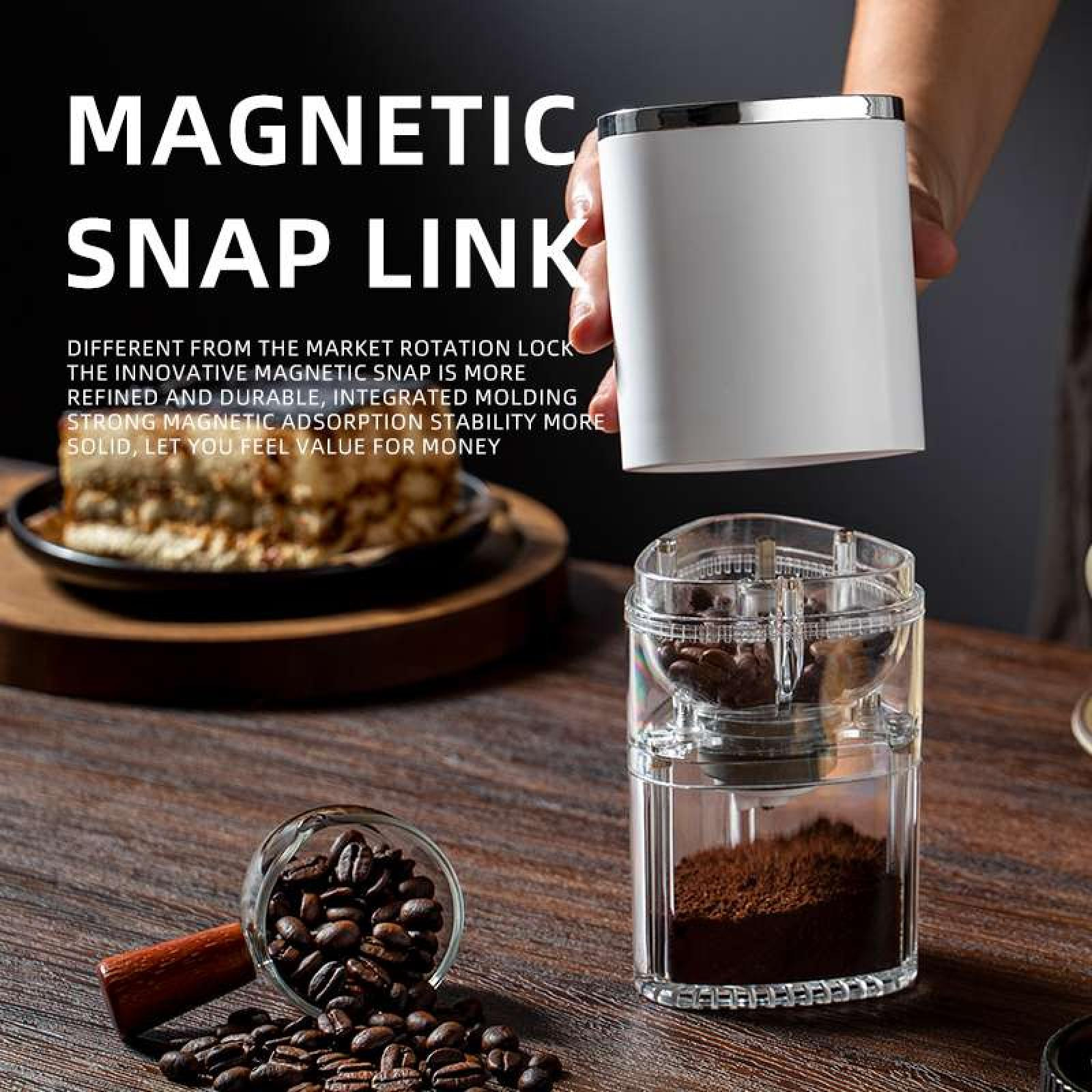 Eine Hand hält einen weißen Zylinder über einer transparenten Kaffeemühle mit Bohnen und gemahlenem Kaffee auf einem Holztisch.