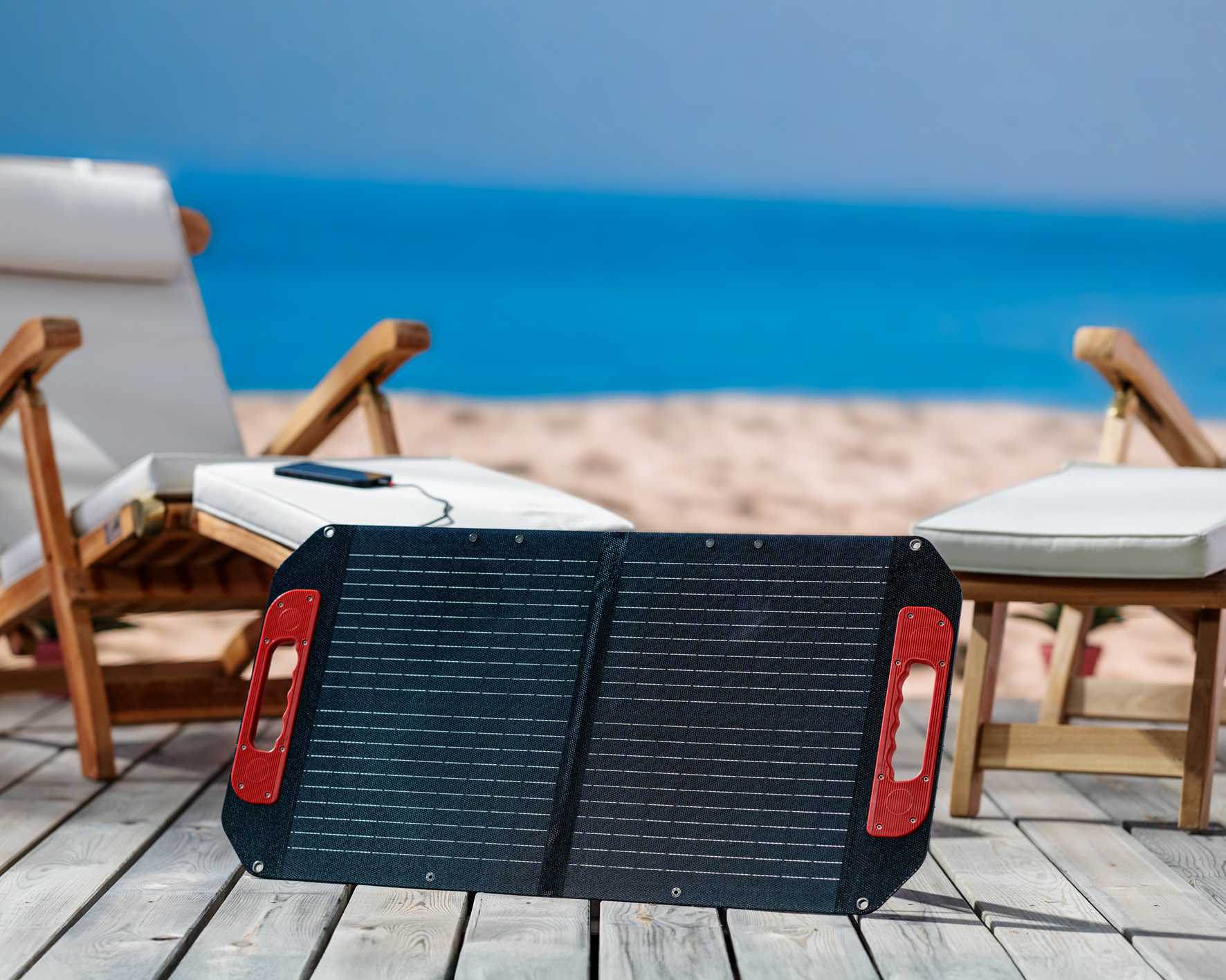 Ein Solarpanel mit roten Griffen liegt auf einem Holzdeck. Strandstühle und das Meer sind im Hintergrund zu sehen.