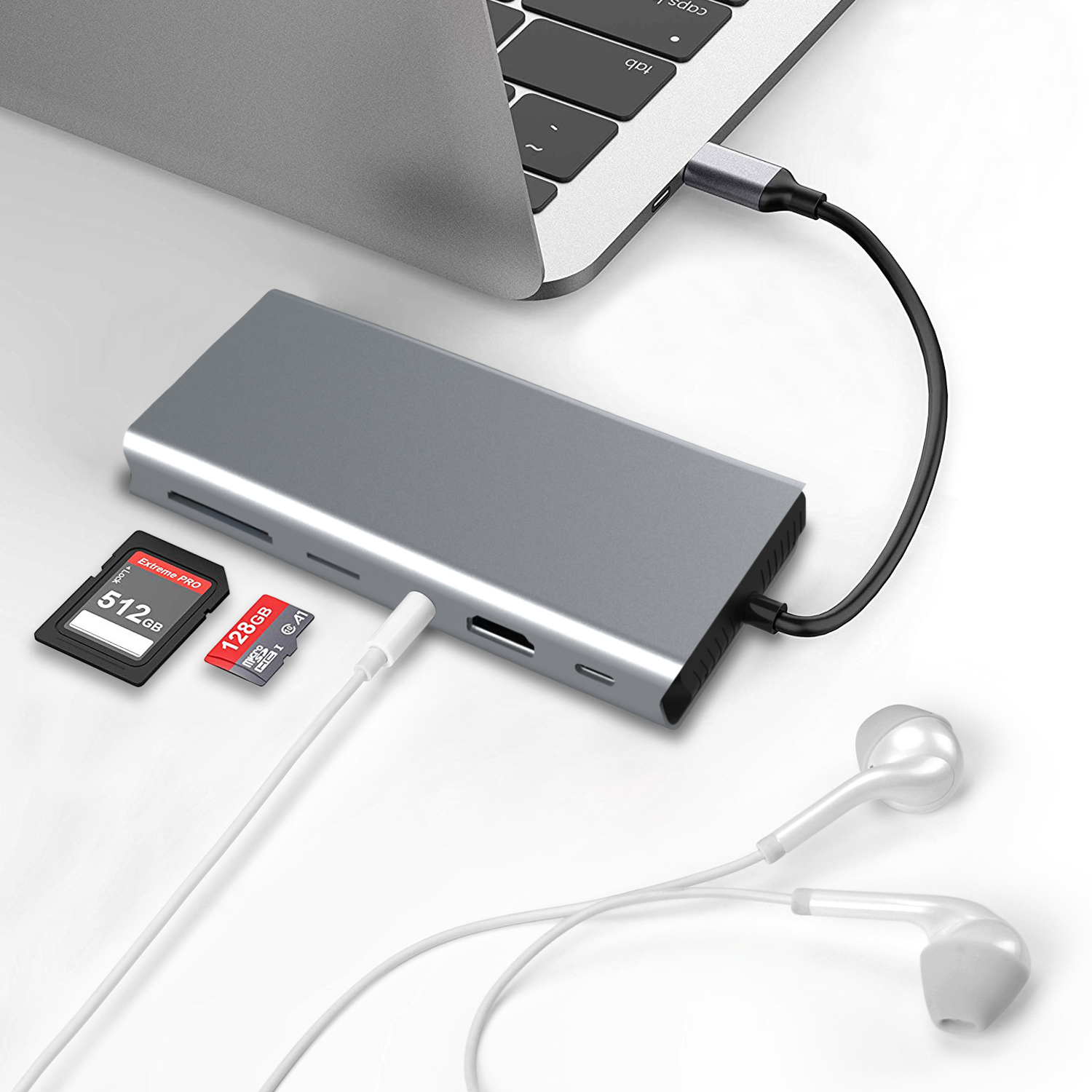 Een zilveren laptop hub met een aangesloten kabel, verbonden met een laptop. SD-kaarten en witte oortelefoons.