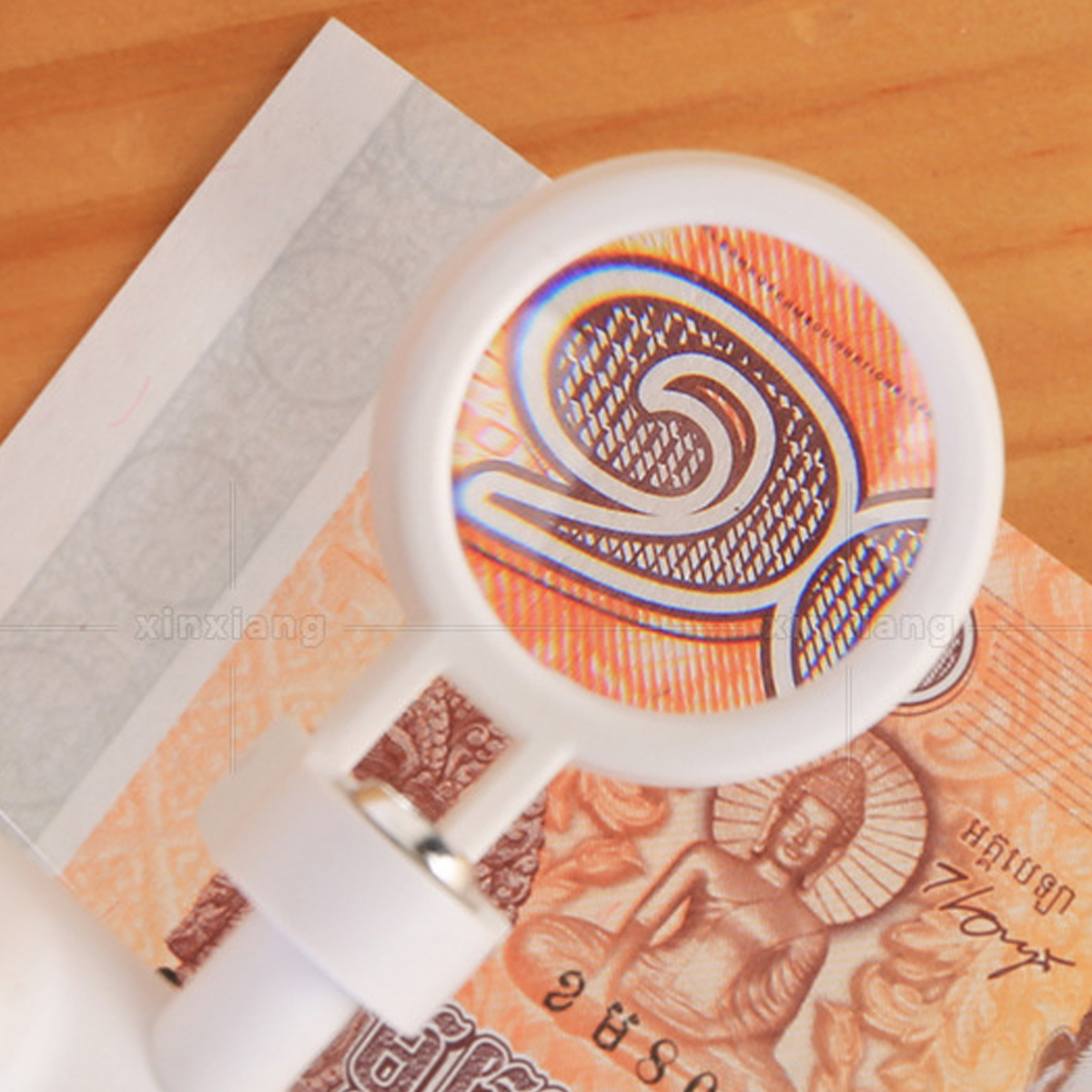 Eine Lupe liegt über einer Banknote. Das Glas zeigt Details der Währung. Der Hintergrund ist eine Holzoberfläche.