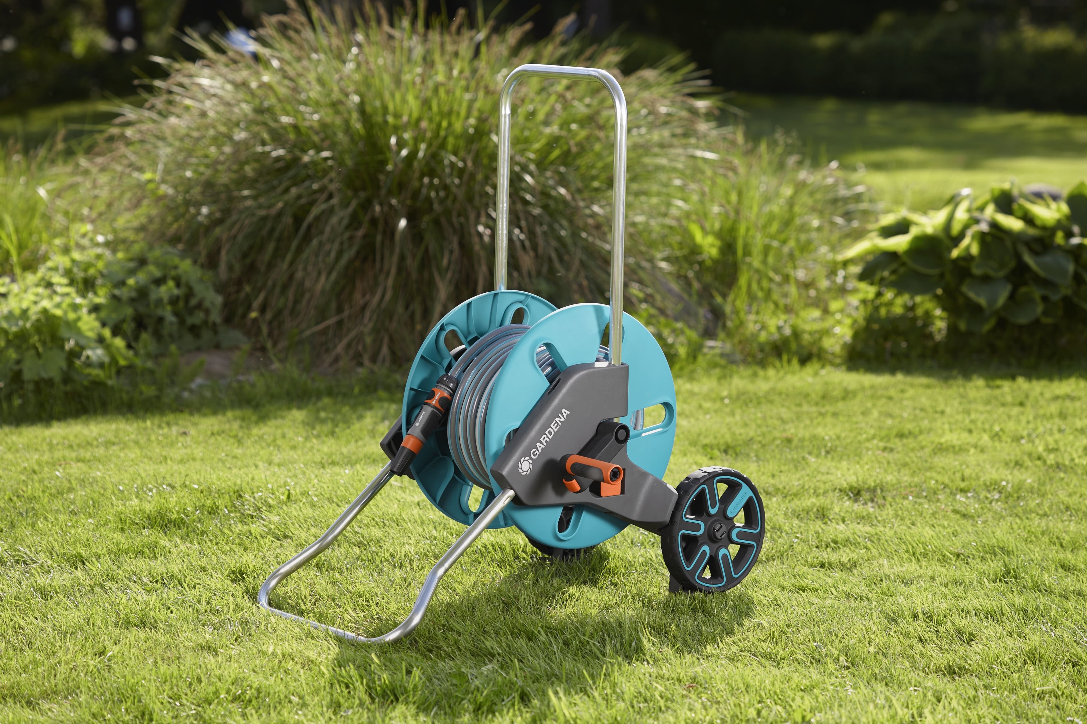 Un avvolgitubo da giardino turchese e grigio è sull'erba. Piante verdi sullo sfondo.