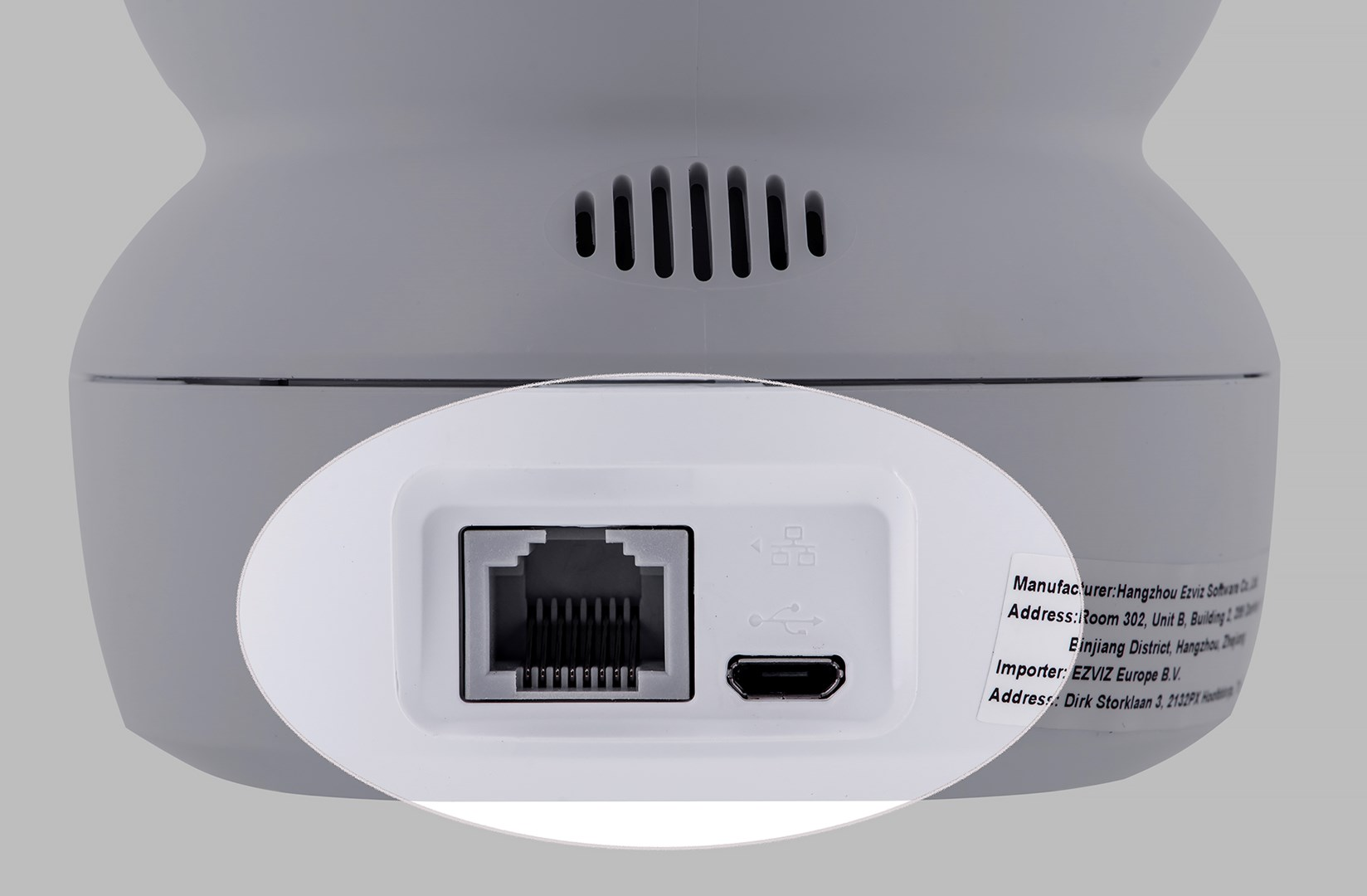 Zbliżenie białego i szarego urządzenia elektronicznego. Pokazuje porty, wentylację i etykiety tekstowe na białej powierzchni.