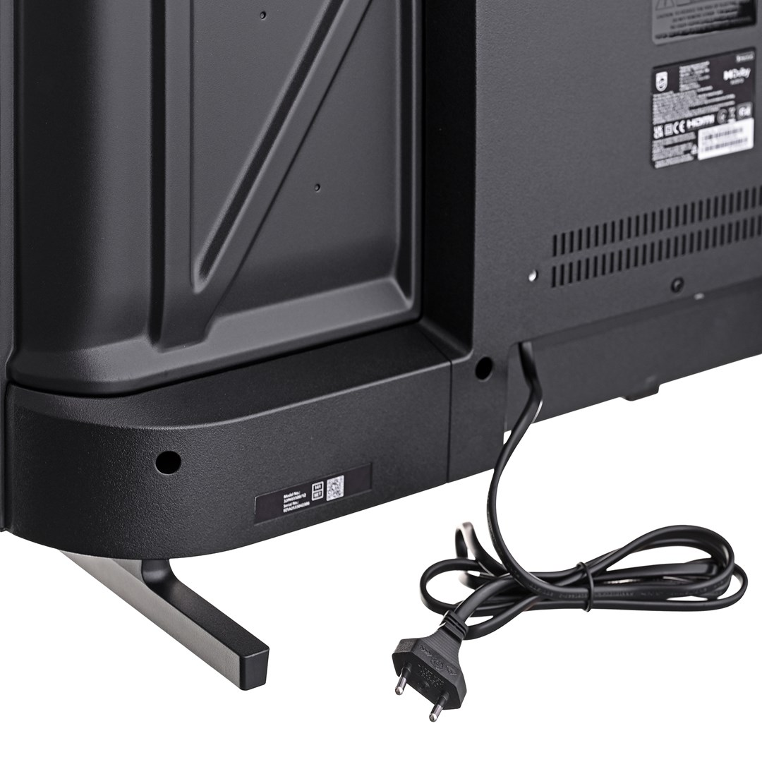 Czarny tył telewizora z kablem zasilającym i wtyczką na białej powierzchni. Telewizor ma metalową podstawę.