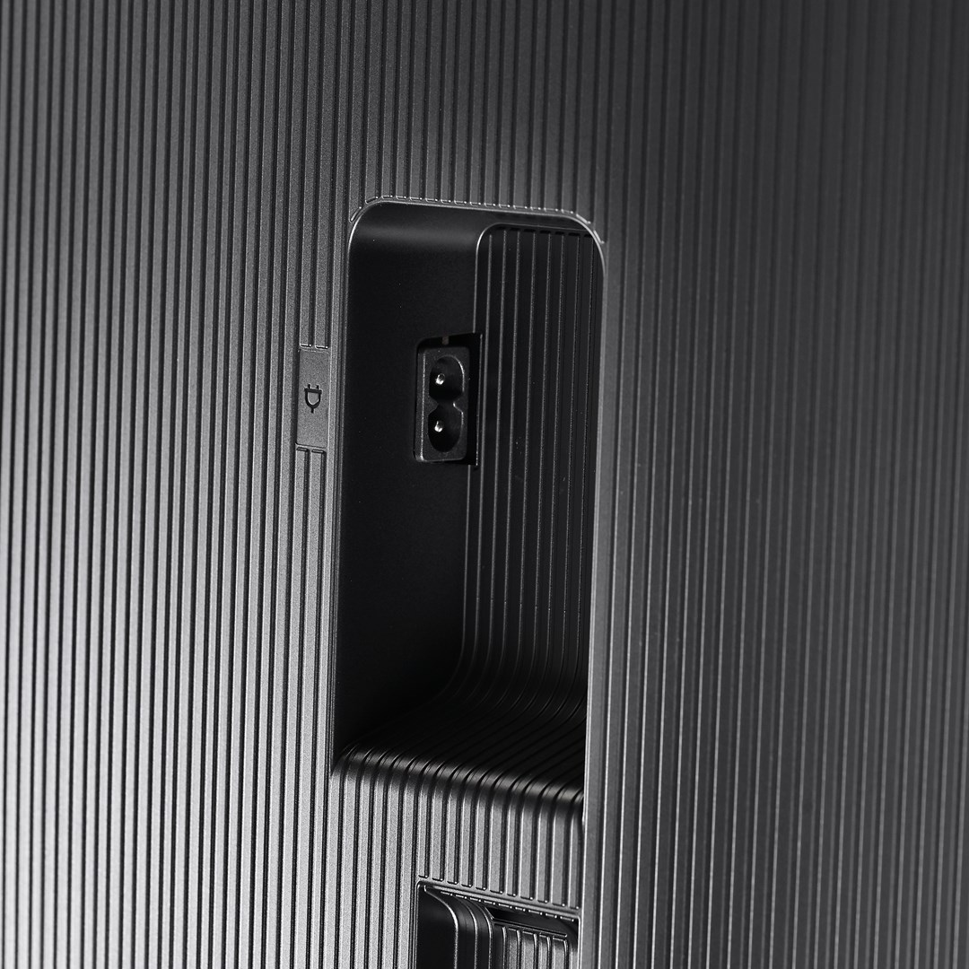 Primo piano del retro di un dispositivo nero. Ha una porta di alimentazione e una superficie strutturata con linee verticali.