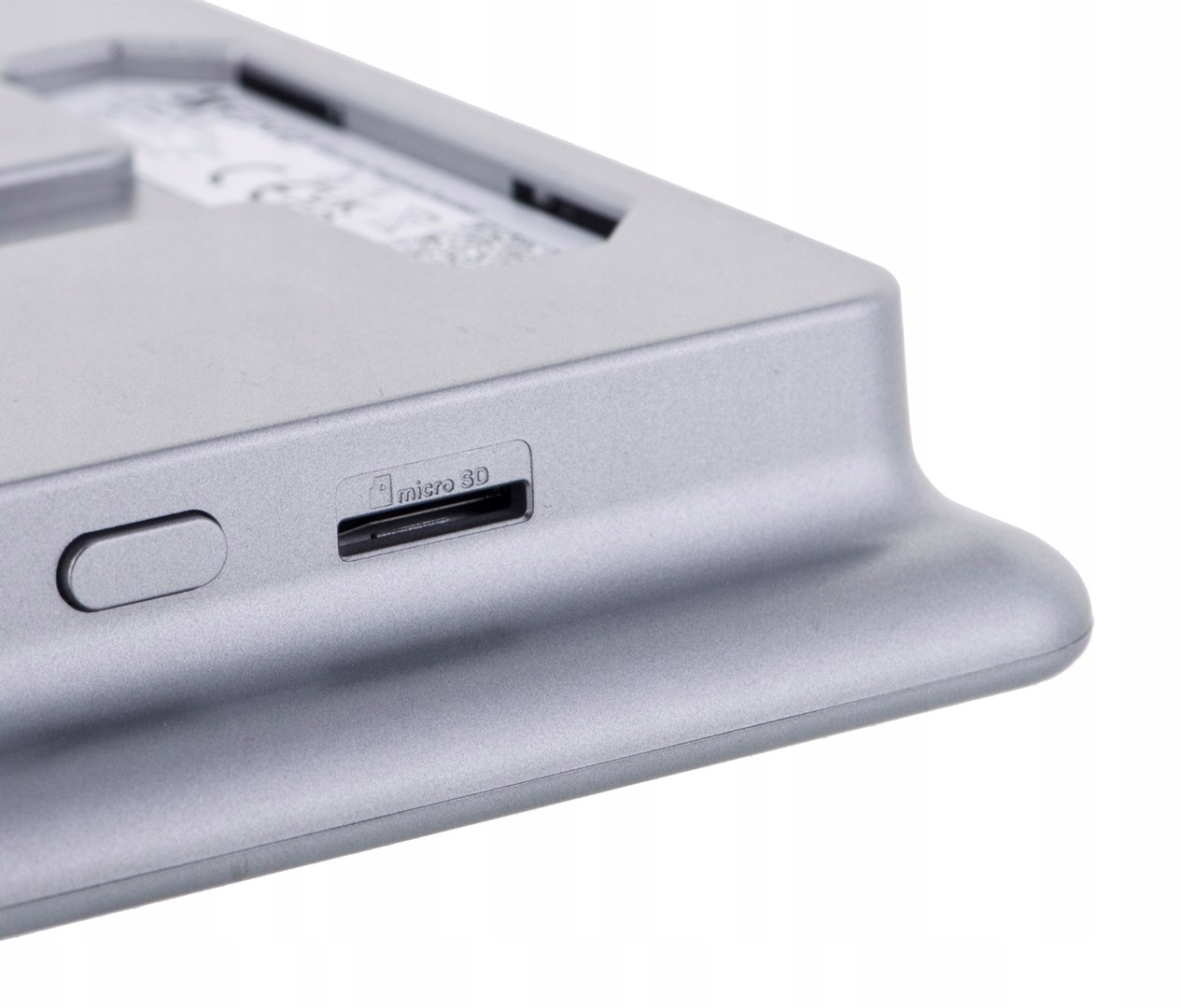 Zbliżenie szarego urządzenia elektronicznego. Widoczny jest slot na kartę Micro SD i przycisk. Tło jest białe.
