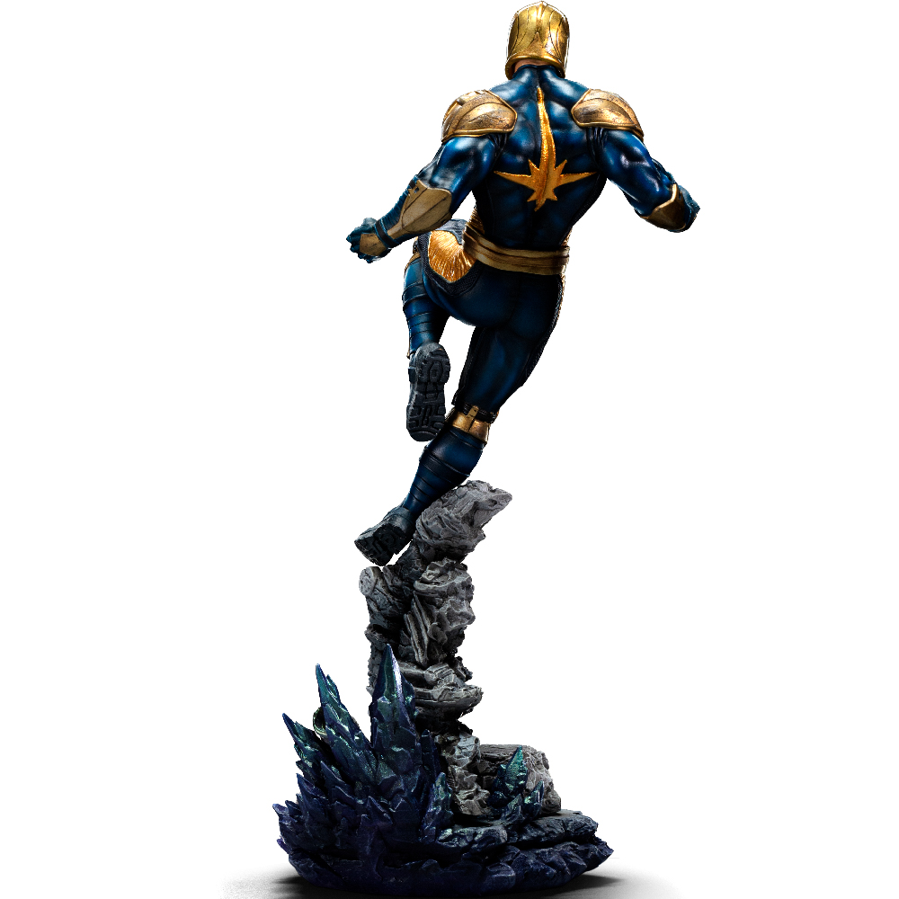 Una statua di un supereroe in tuta blu e oro salta da una base rocciosa, con una stella sulla schiena e un elmo dorato.
