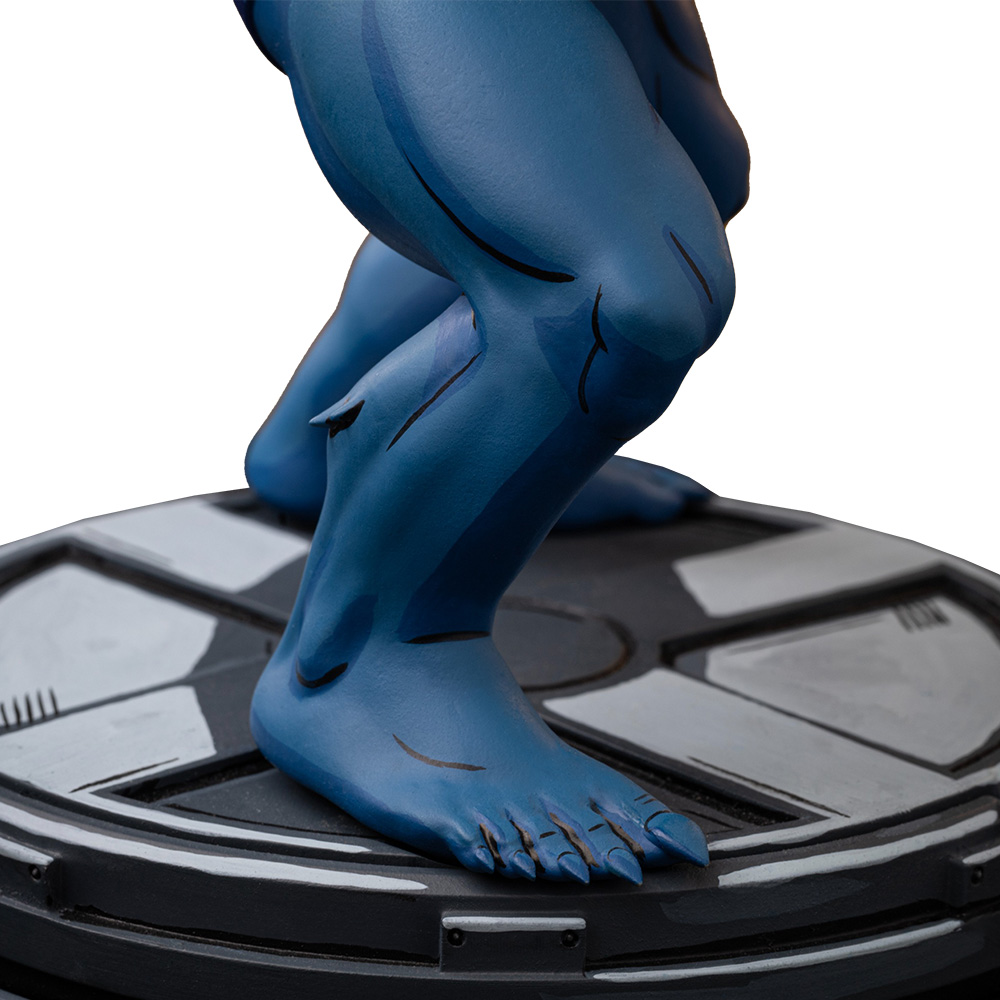 Eine blaue Statue der Beine und Füße einer Person, die auf einer grau-schwarzen Plattform posiert. Die Haut hat dunklere blaue Markierungen. Der Hintergrund ist weiß.