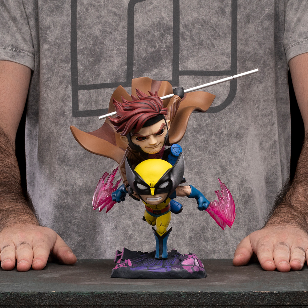 Una statuetta di Gambit che trasporta Wolverine è in mostra. Lo sfondo è una maglietta grigia con un logo. Mani su entrambi i lati della statuetta.