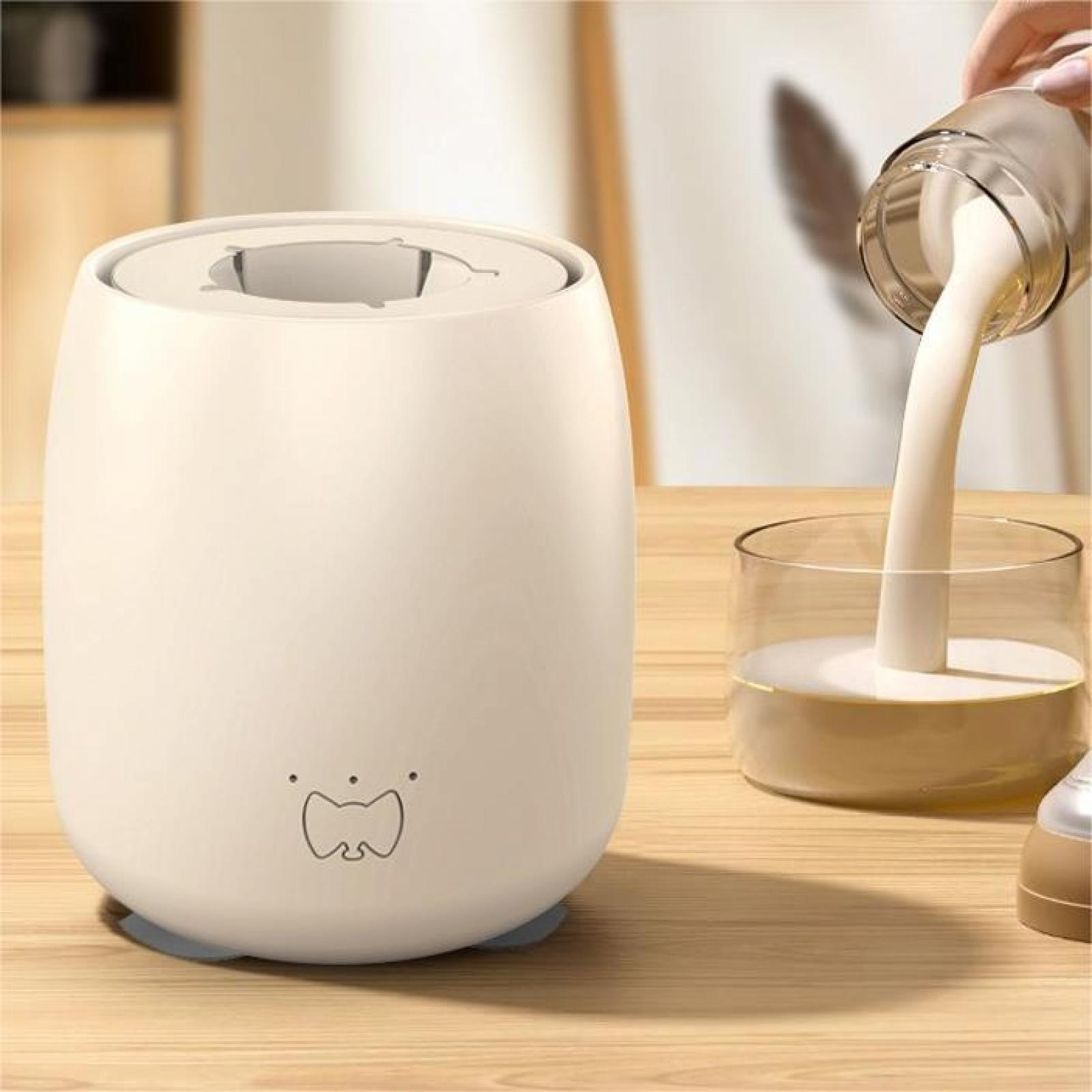 Ein weißer Babyflaschenwärmer. Milch wird in ein Glas gegossen. Es steht auf einem Holztisch.