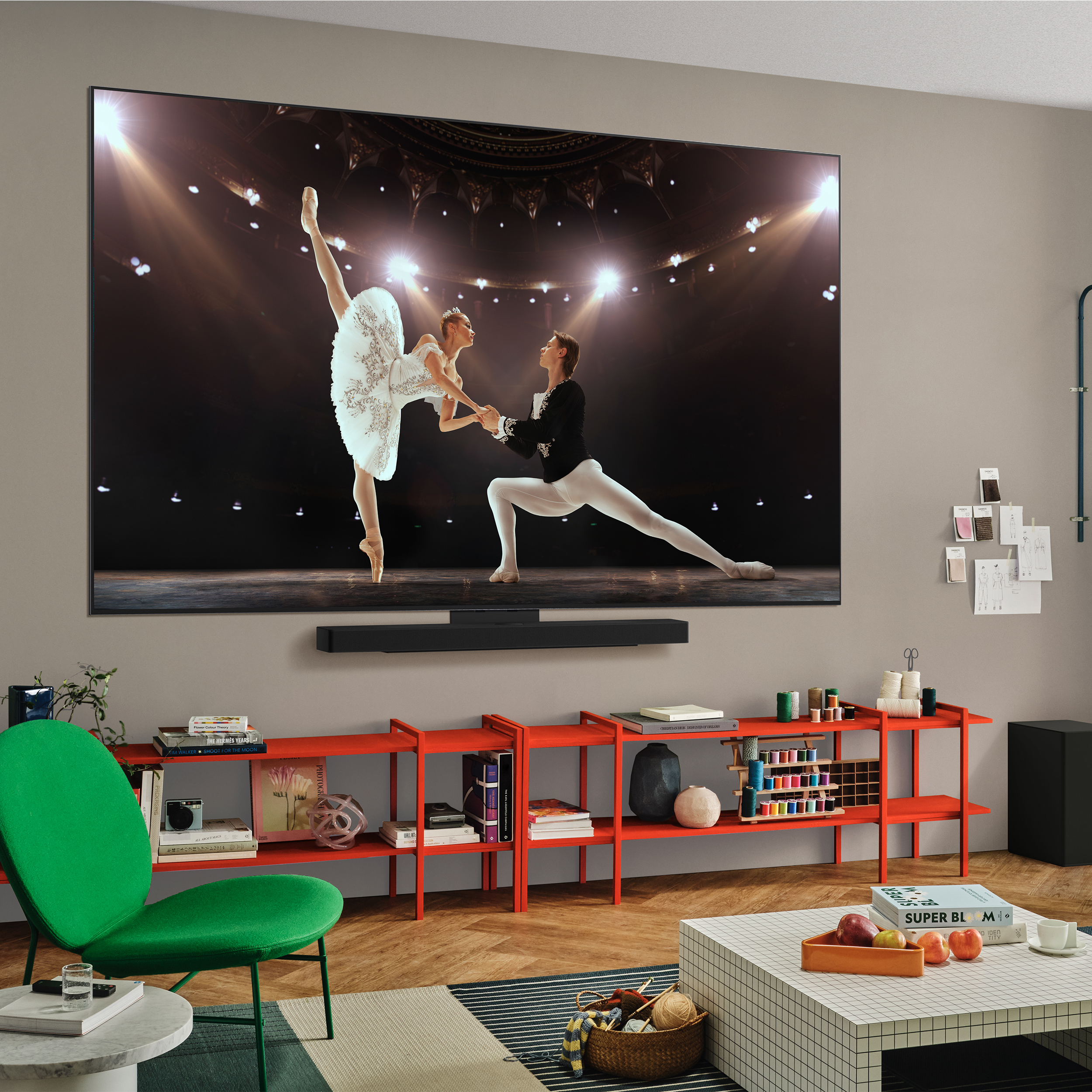 Un salon avec une grande télévision montrant du ballet. Des étagères rouges contiennent des objets. Une chaise verte est au premier plan.