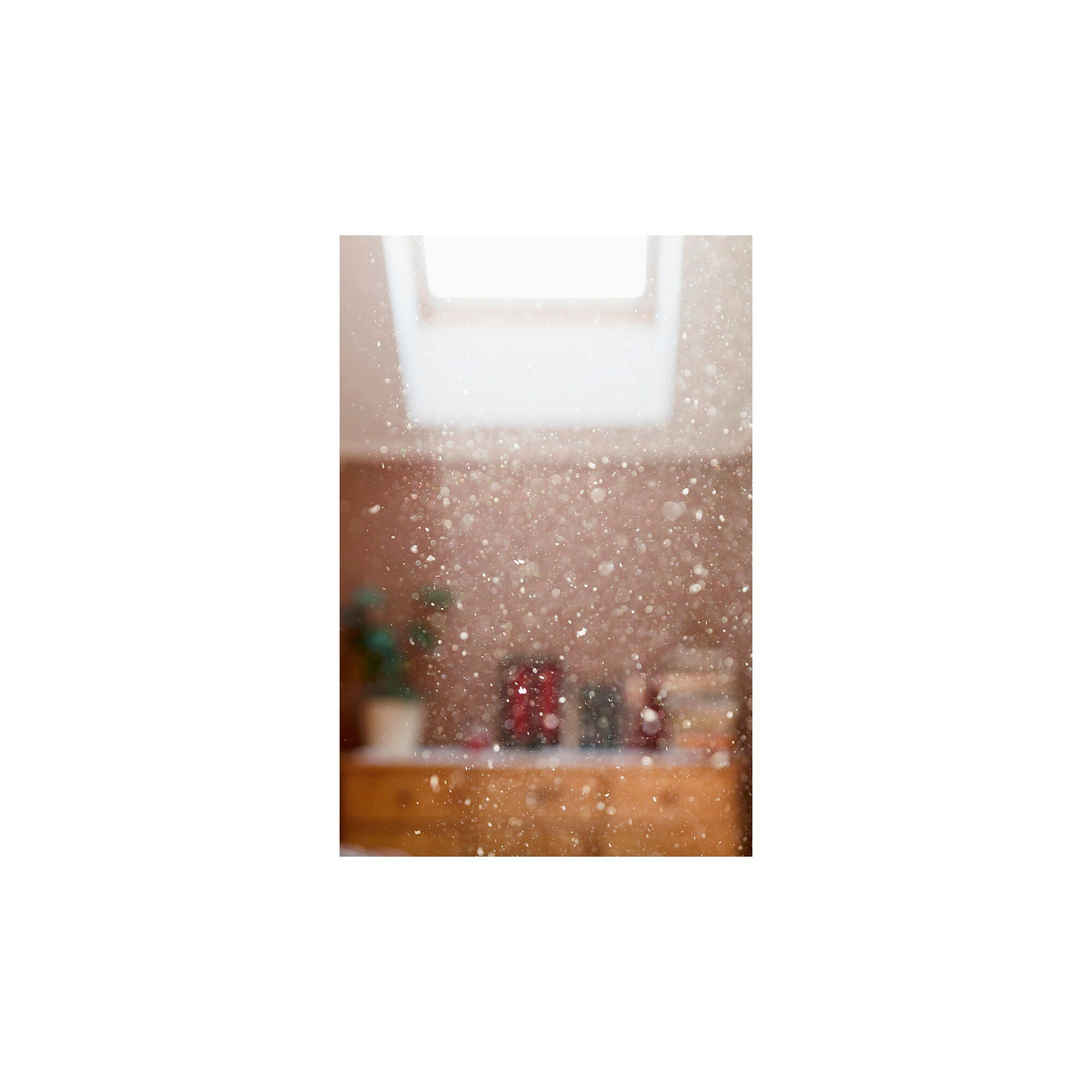 Cząsteczki kurzu w powietrzu, z jasnym świetlikiem. Książki i dekoracje na drewnianej szafce są lekko widoczne.