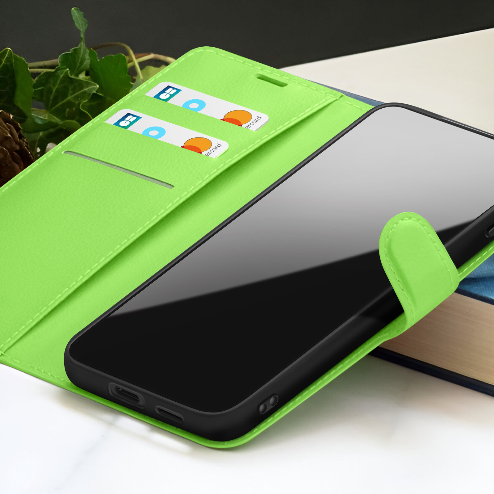 Un étui de téléphone vert avec un téléphone noir à l'intérieur. Des cartes de crédit sont visibles dans l'étui. Un livre en arrière-plan.