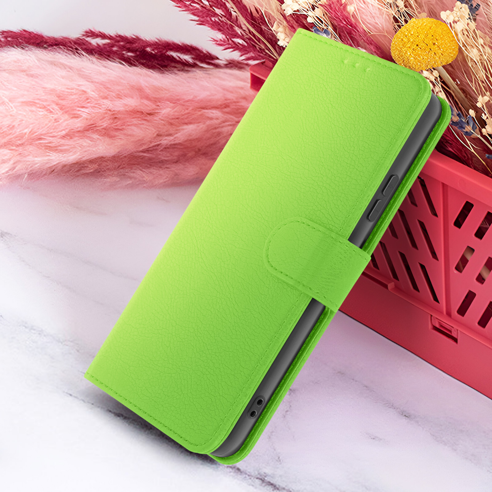 Un étui de téléphone vert repose sur une surface en marbre, à côté d'éléments décoratifs roses et bordeaux et d'un conteneur rouge.