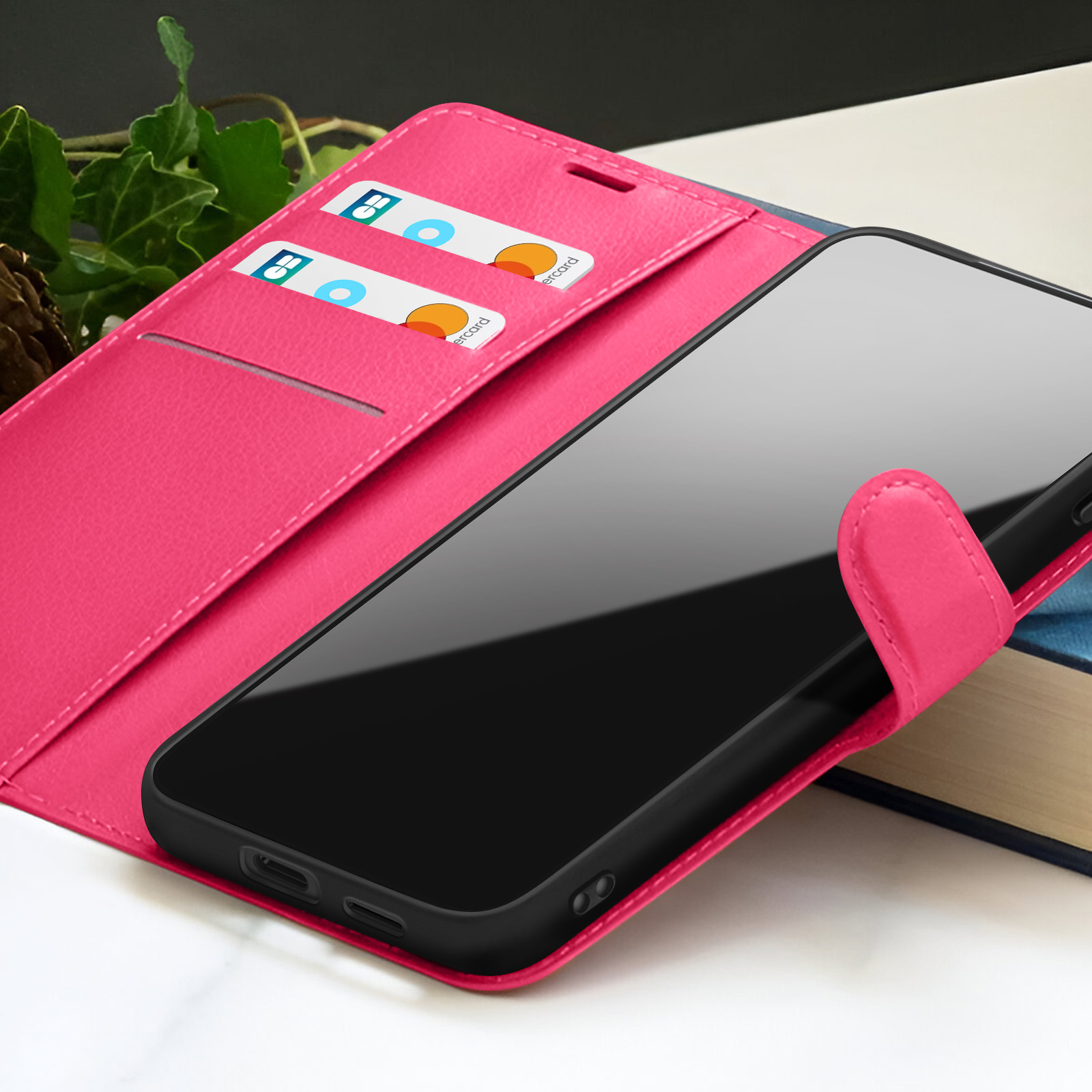 Een roze telefoonhoesje met een smartphone. Creditcards zitten in de hoes. Boeken op de achtergrond.