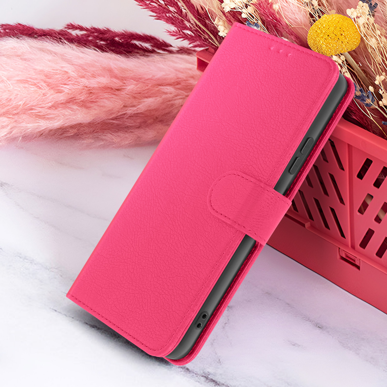 Roze telefoonhoesje met een textuur, een roze bak en roze en gele decoratieve elementen op een marmeren oppervlak.