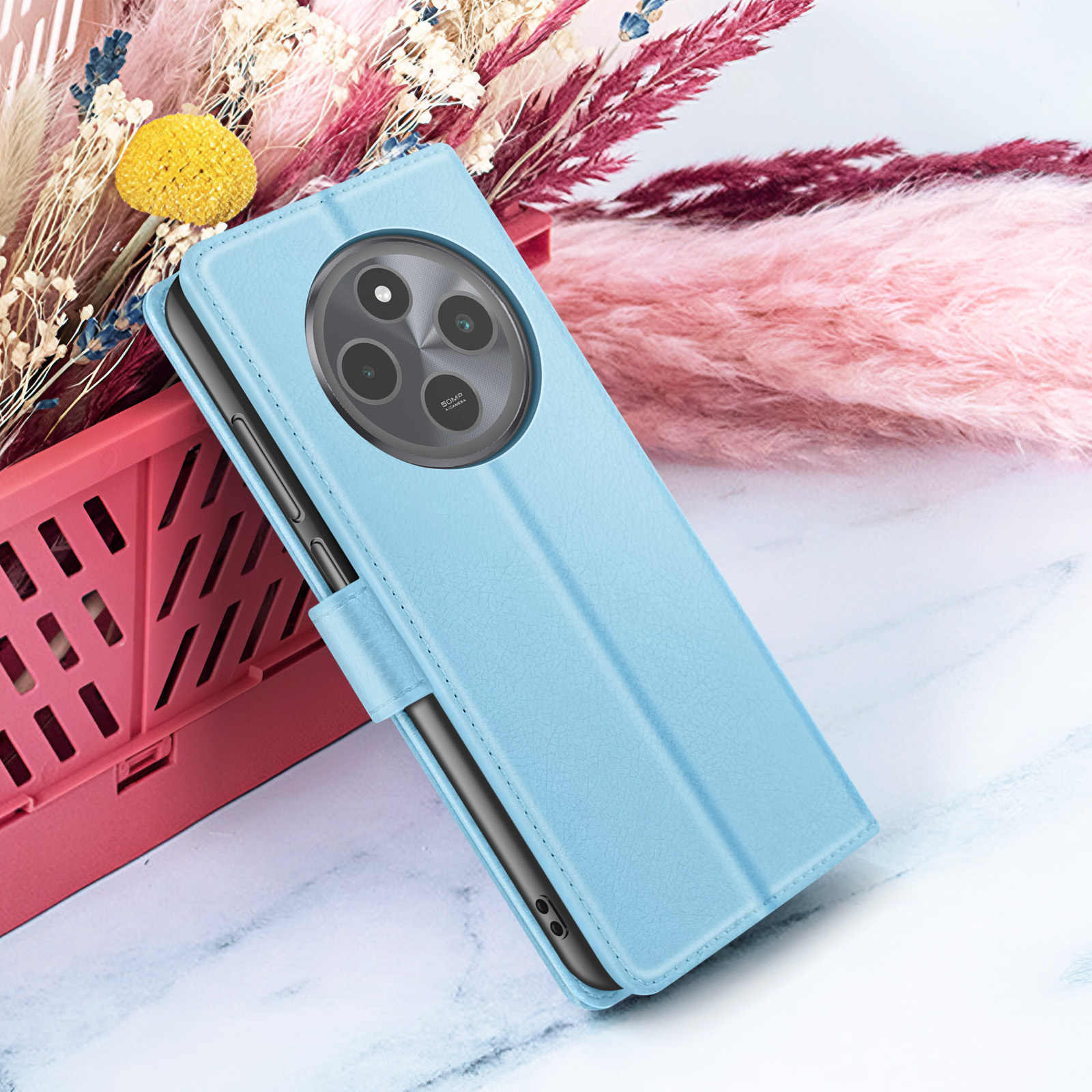 Een lichtblauwe telefoonhoes met een rond cameradesign, tegen een achtergrond van roze en beige gedroogde bloemen.