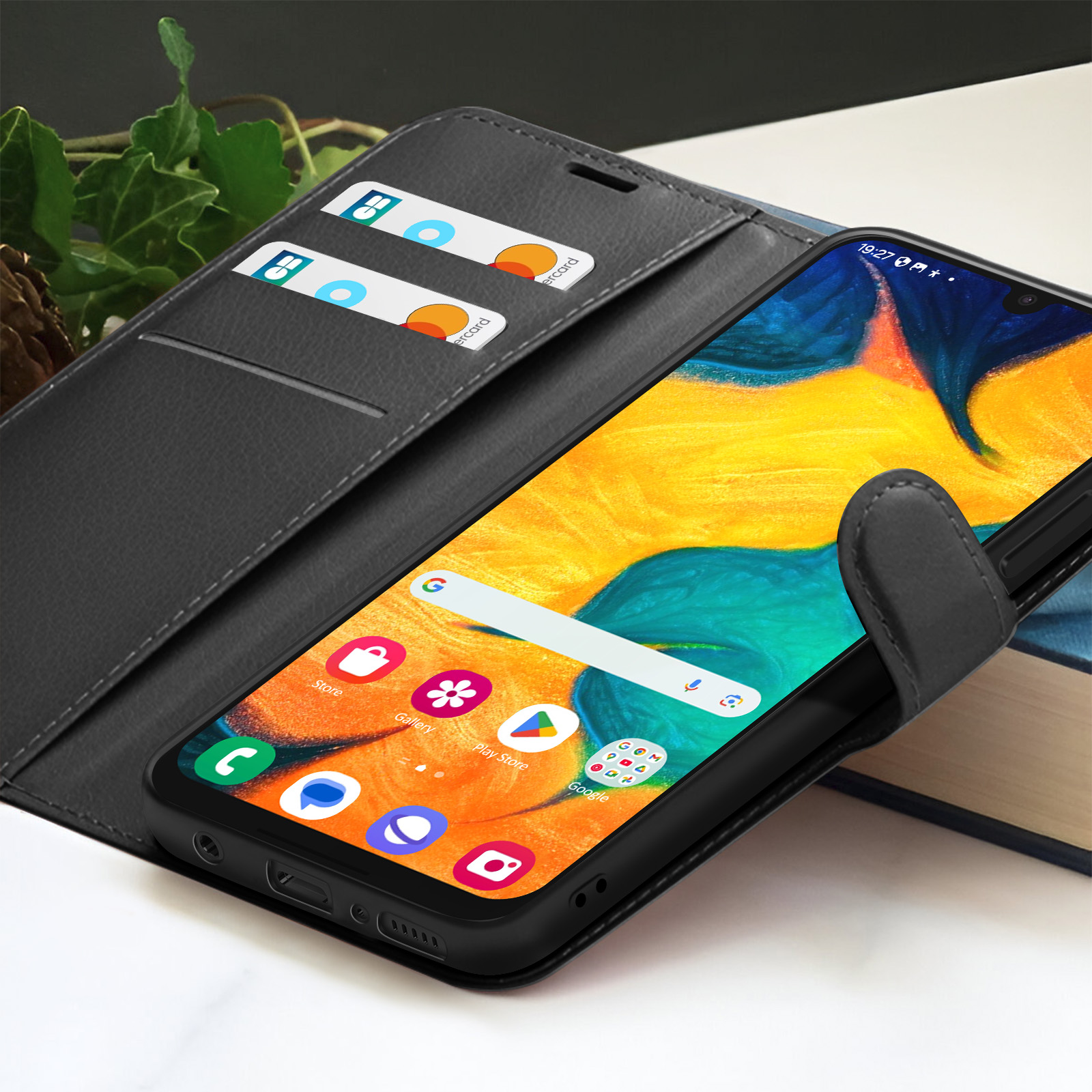 Un smartphone dans un étui noir affiche son écran avec des applications. Cartes de crédit dans l'étui. Le téléphone est sur un livre.
