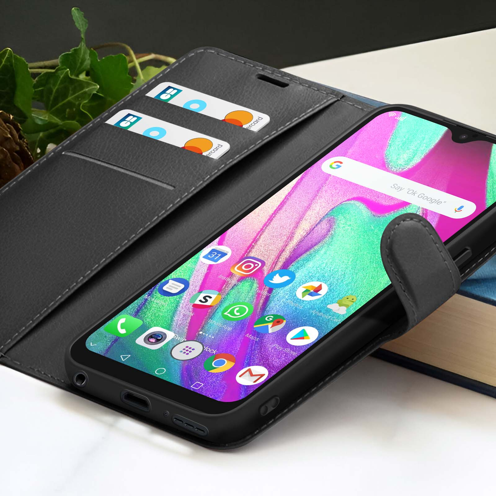 Un smartphone dans un étui noir, affichant un écran coloré avec des applications. Cartes de crédit dans l'étui. Un livre à l'arrière.
