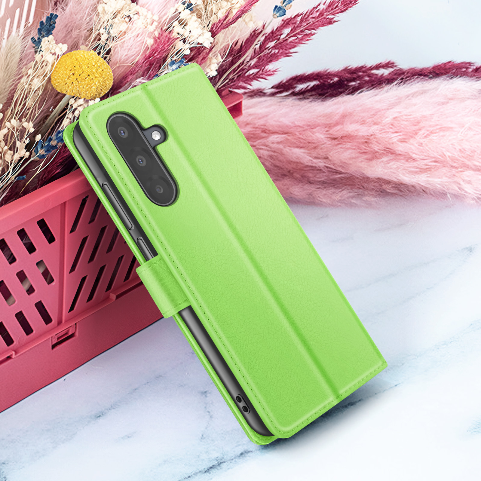 Een groene telefoonhoes is open en toont een telefoon. Roze en witte bloemen op de achtergrond.