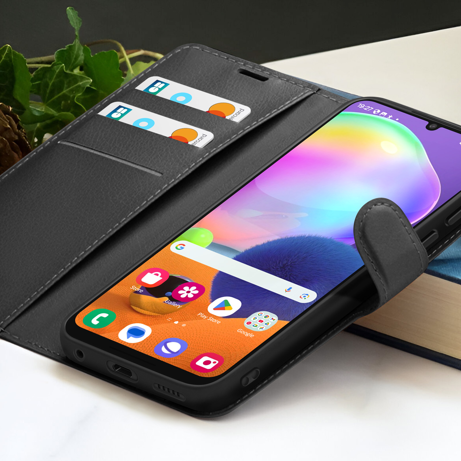 Un smartphone dans un étui en cuir noir avec des cartes dans la poche. L'écran affiche des icônes. L'arrière-plan comprend un livre et des feuilles.