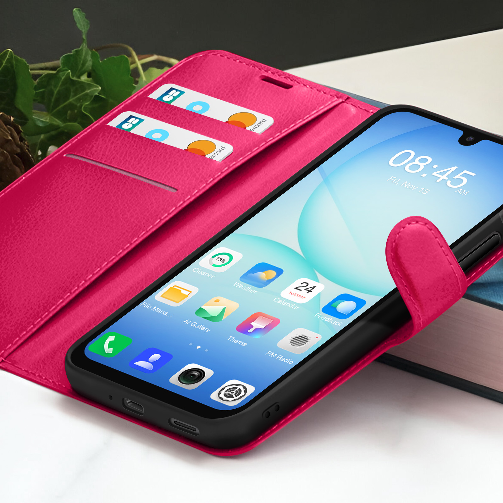 Een roze telefoonhoesje met een telefoon die de tijd weergeeft. Er zitten kaarten in het hoesje. De achtergrond heeft groen en een boek.