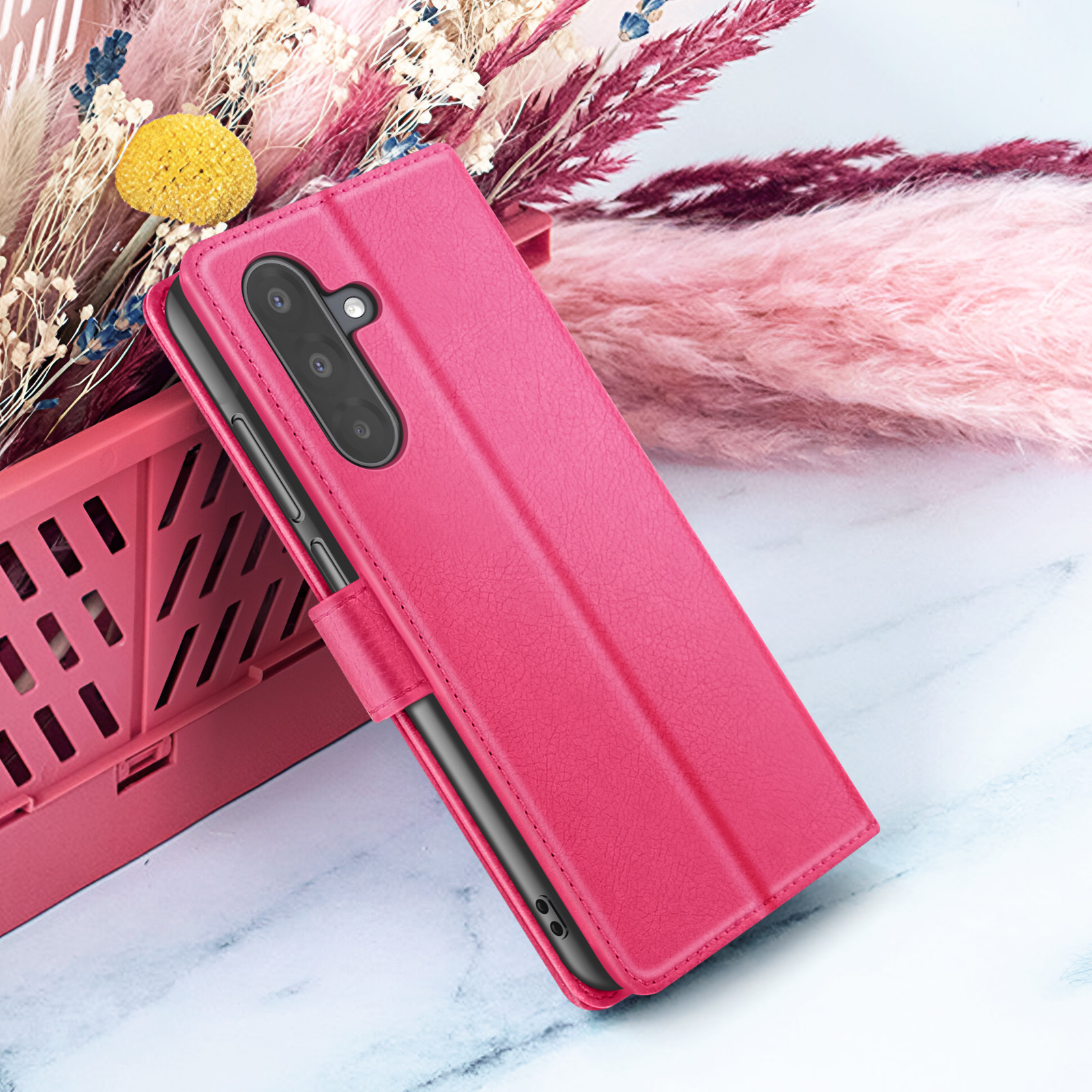 Een roze telefoonhoesje is open en onthult een zwarte telefoon. Achtergrond heeft roze en witte bloemen.