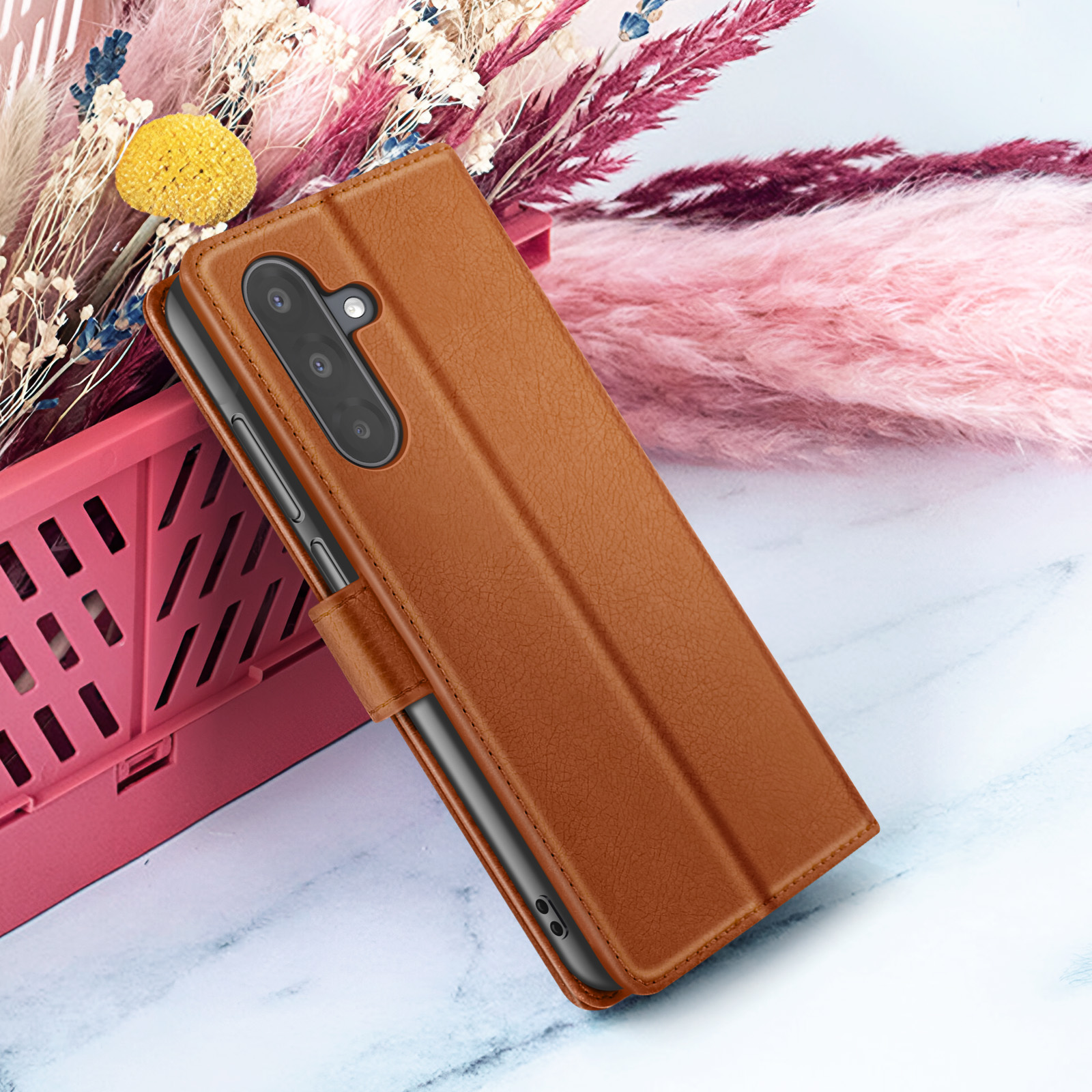 Bruine leren telefoonhoes met een telefoon erin, geplaatst voor bloemen en een lichte achtergrond.