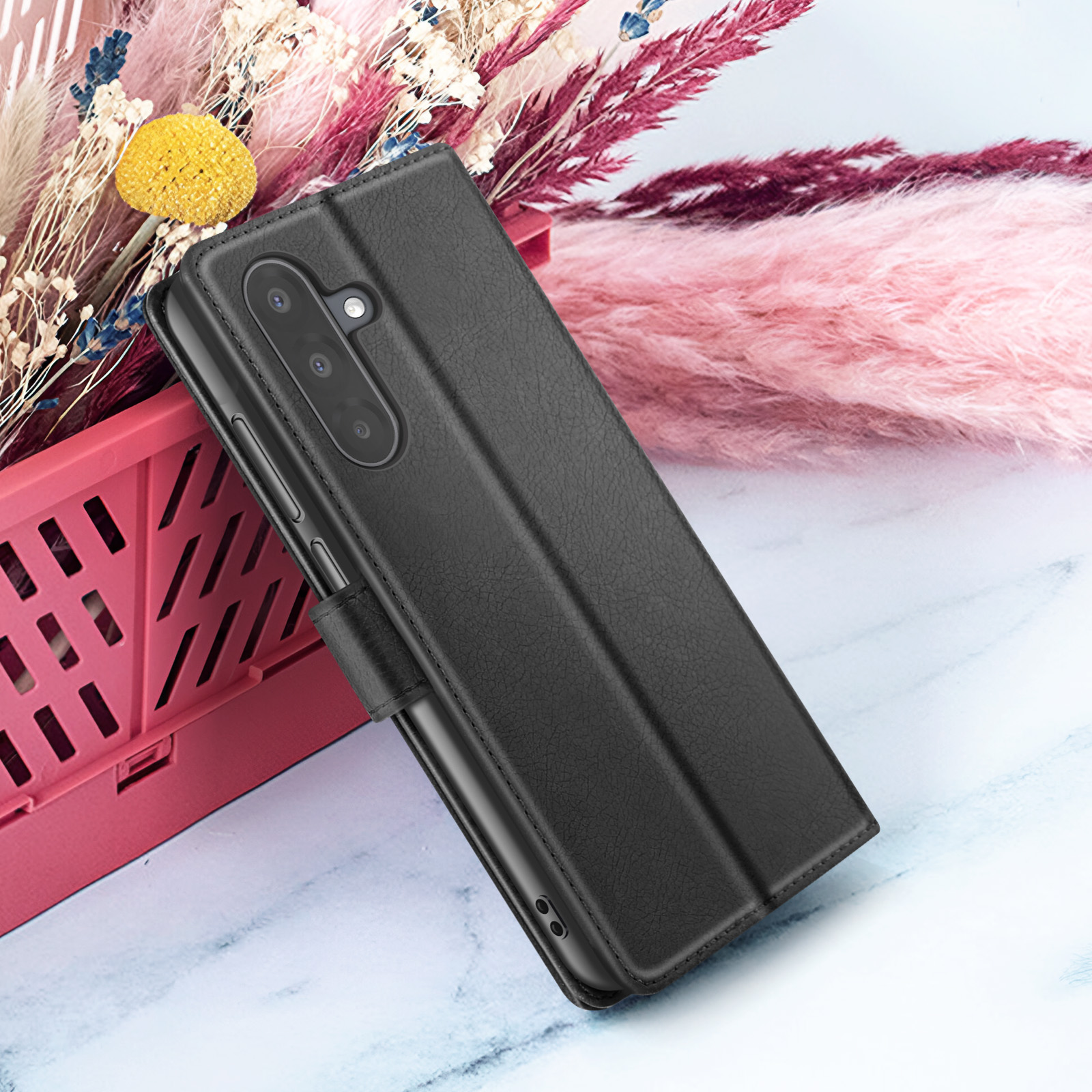 Zwarte telefoonhoes met een getextureerde afwerking, geplaatst naast een roze en wit bloemstuk, op een marmeren oppervlak.